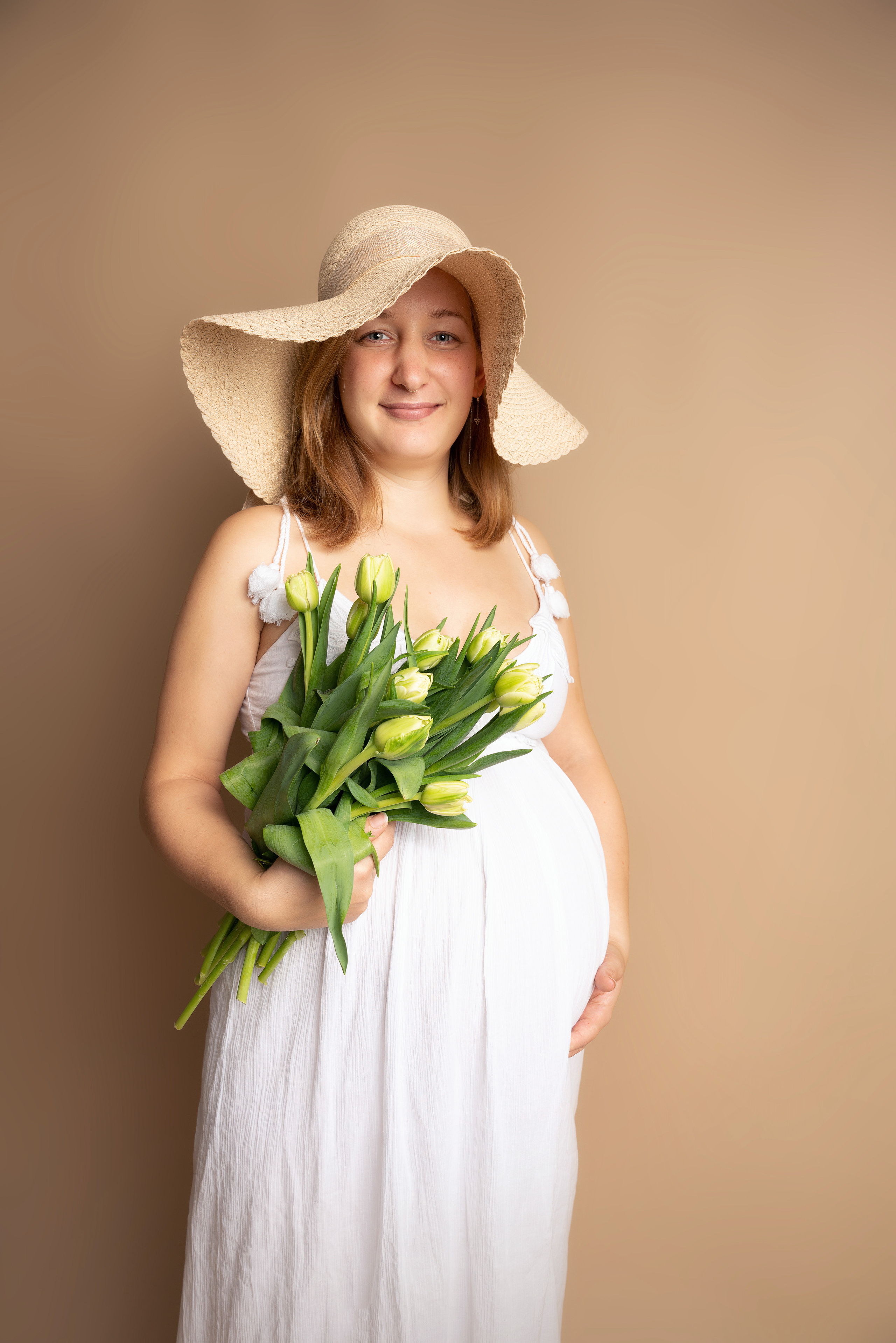 Eine Frau trägt ein hübsches Kleid und posiert stolz mit ihrem Babybauch