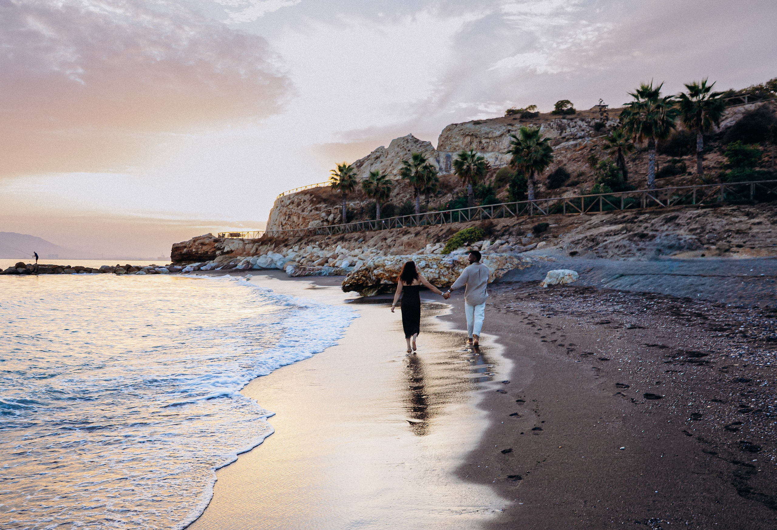Destination engagement photography in Málaga showing the couple walking along the shoreline after their beach proposal. Soft evening tones and coastal scenery create a timeless Mediterranean love story atmosphere.