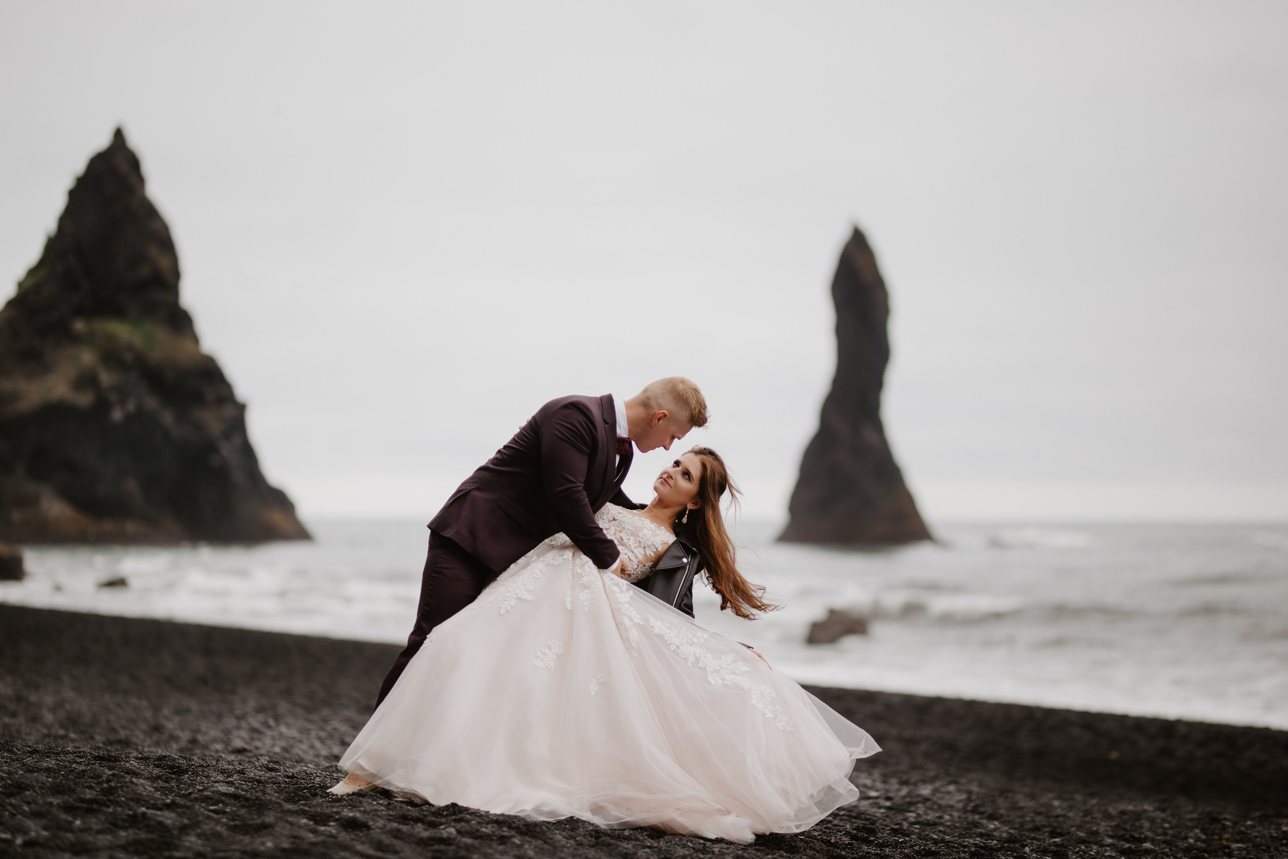 Love and adventure—couple walking along Reynisfjara Beach, Iceland, with the Reynisdrangar sea stacks in the distance.