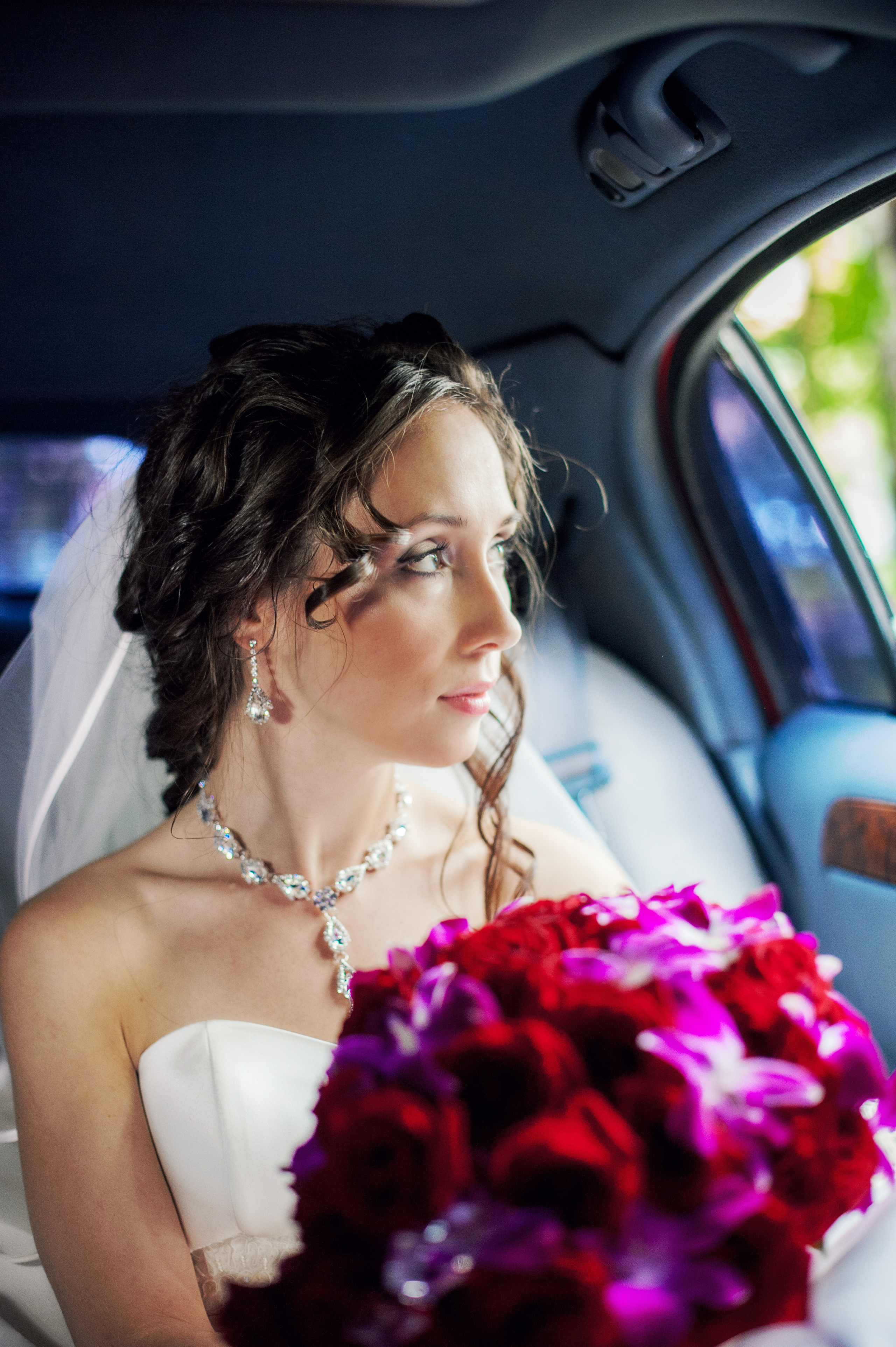 Свадебная фотосессия в Москве. Невеста сидит в свадебном автомобиле у открытого окна с фиолетовым букетом цветов