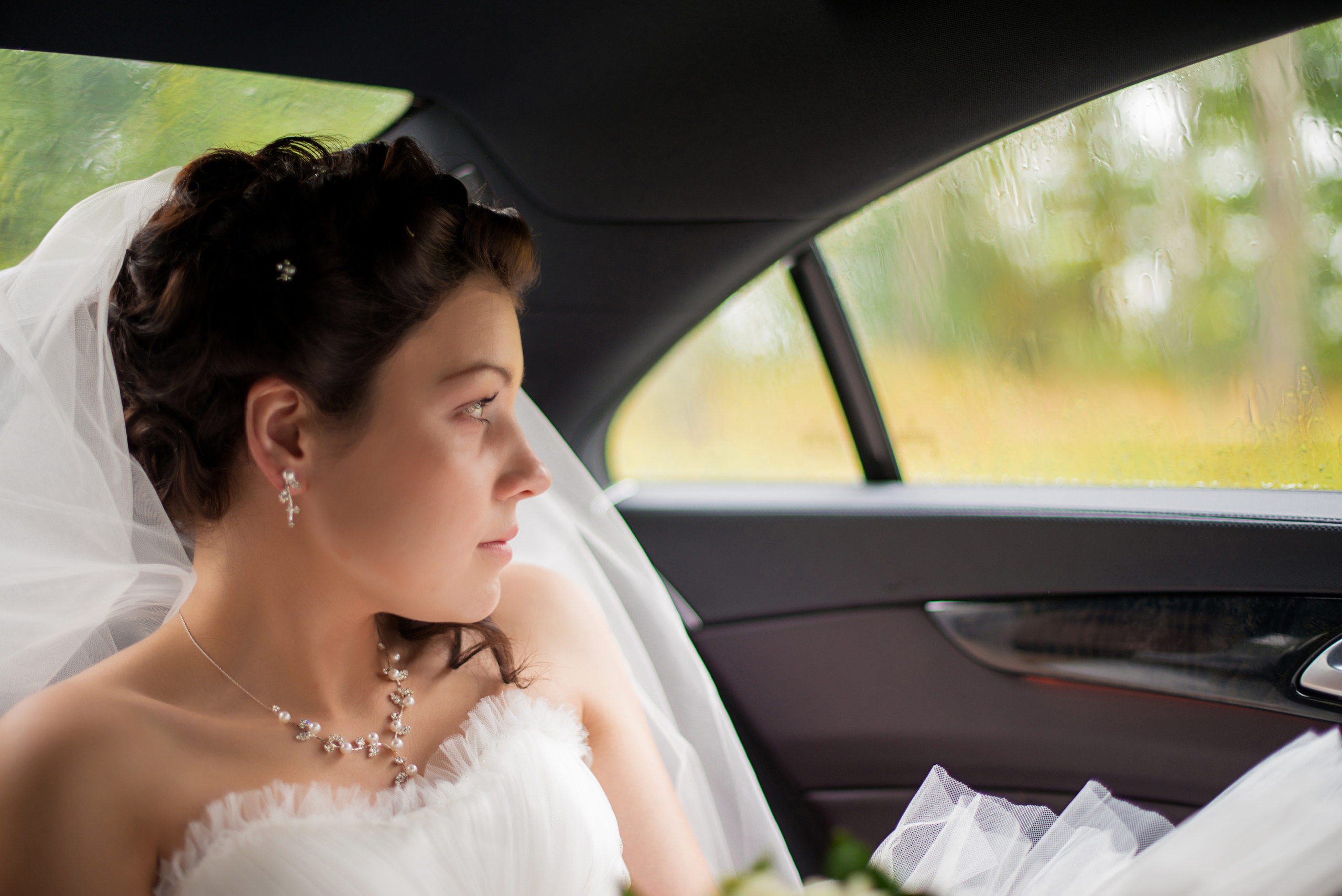 Свадебная фотосессия в Москве. Невеста сидит в свадебном автомобиле у окна, на улице идет дождь, поэтому невеста грустит