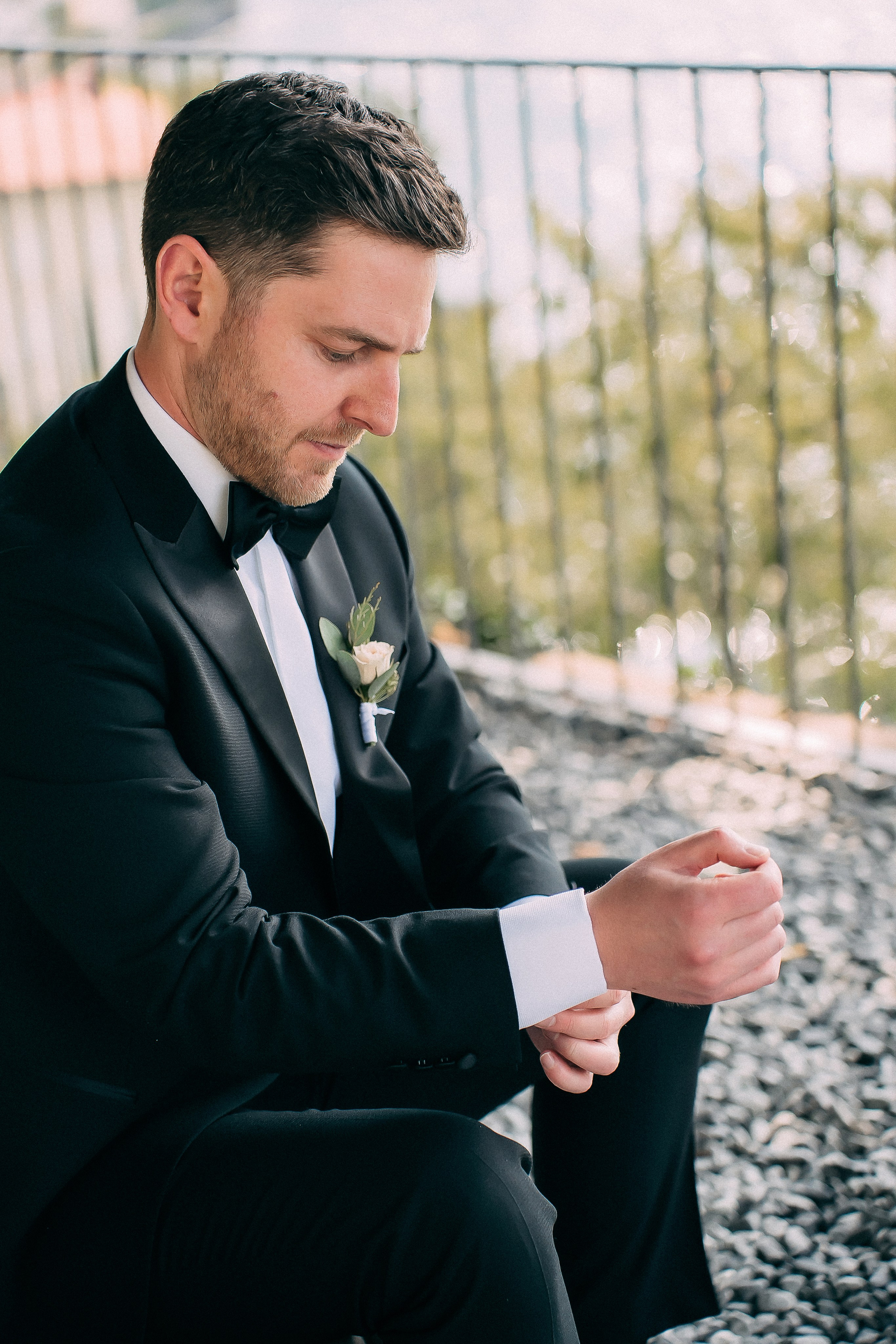 Groom sitting on a stone wall with Lake Como in the background at Villa Lario, Italy