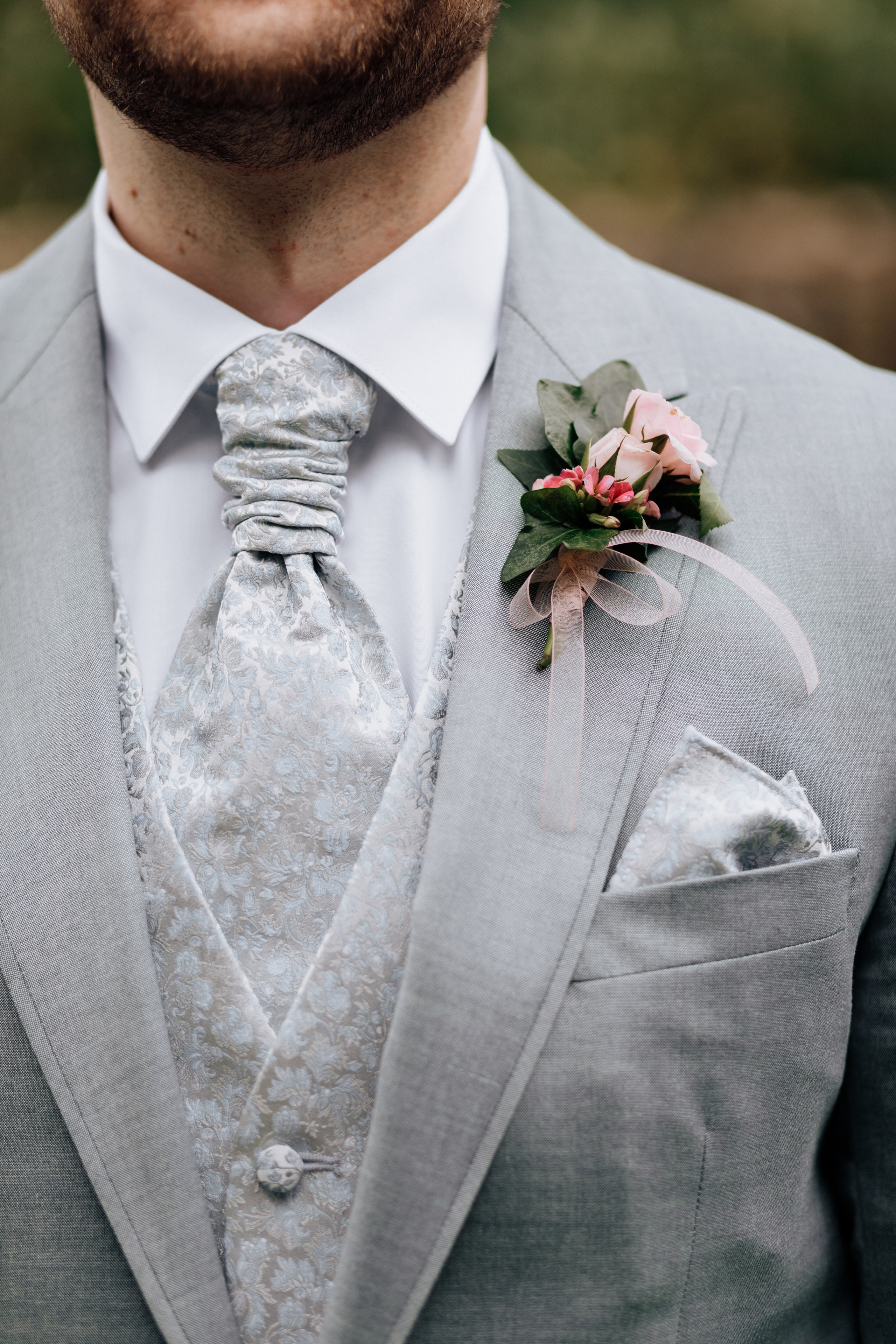 Details des Hochzeitsanzugs des Bräutigams: Krawatte, Weste, Anstecker und Taschentuch im Sakko. Ein elegantes Detail.