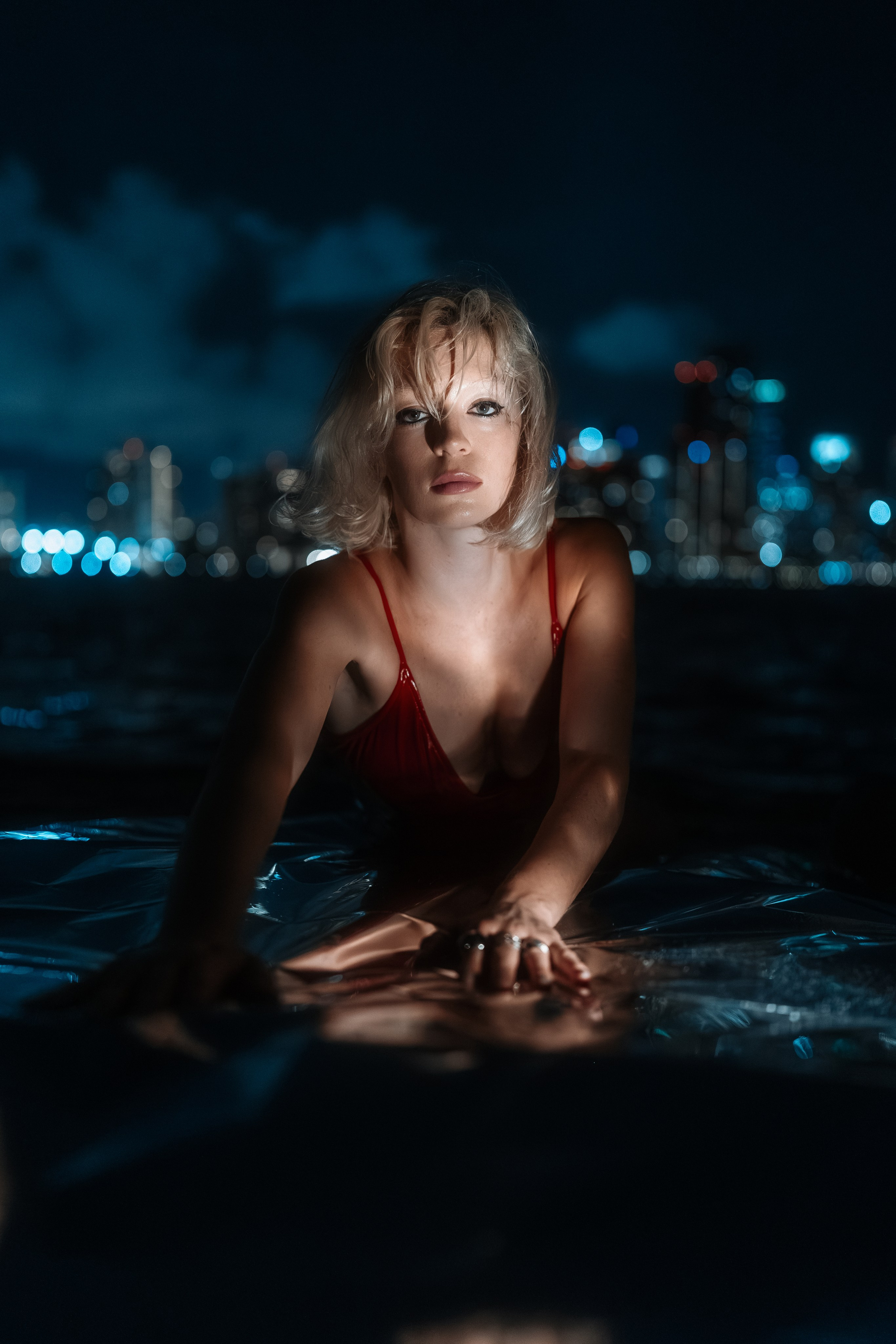 Silhouette by the water with city lights blurred in the background. Clean composition with emphasis on body shape.
