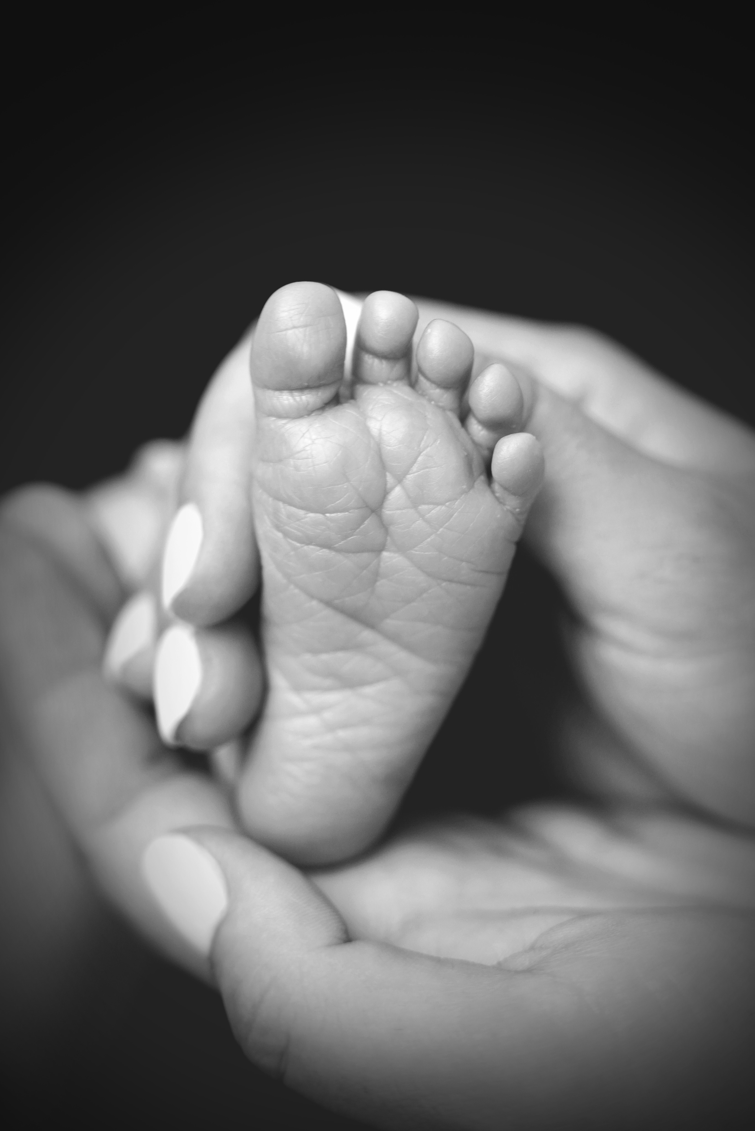 Schwarz-Weiß-Fotografie der Fersen eines Babys in den Händen der Mutter