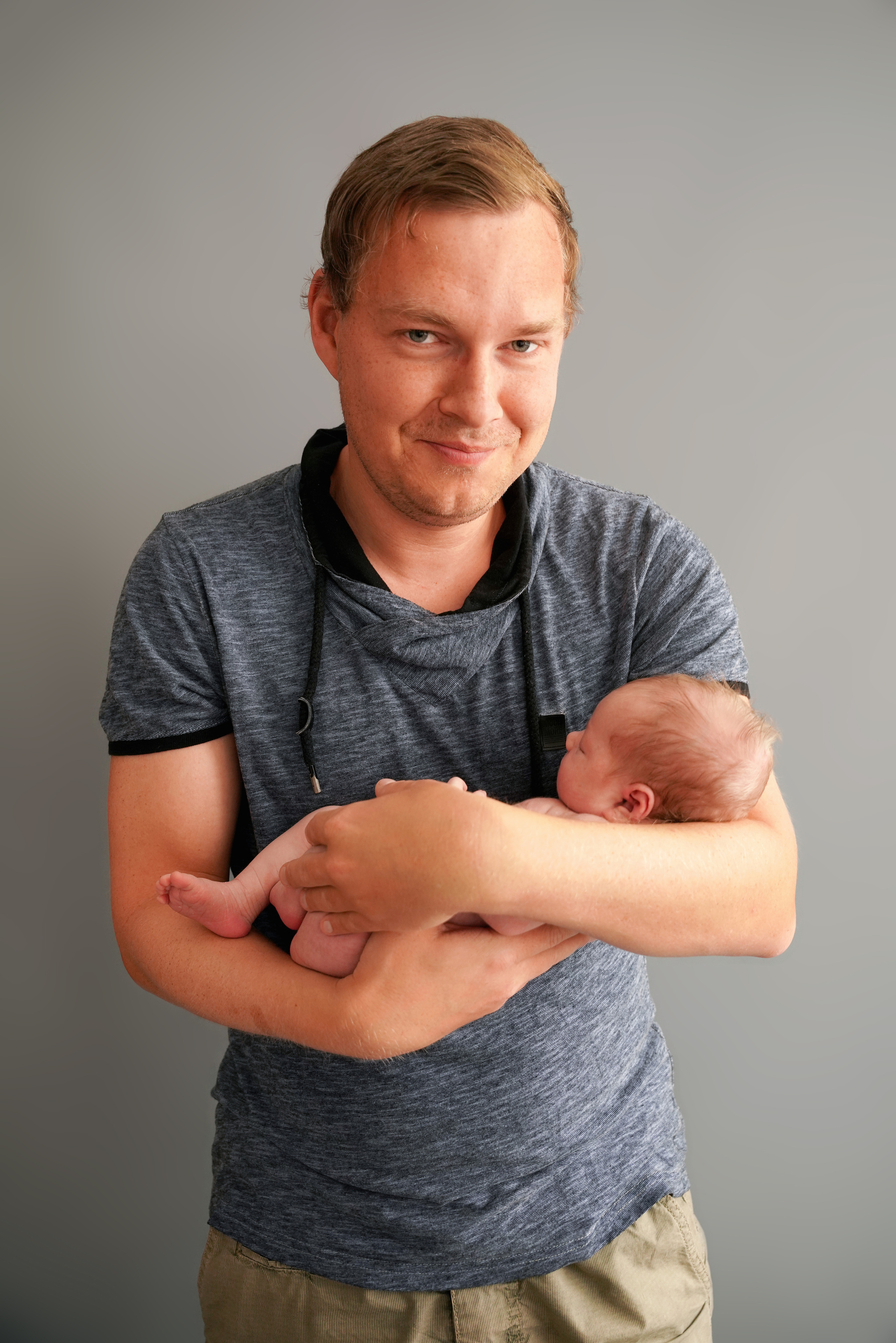 Vater lächelt mit seiner Tochter im Arm in die Kamera blickend