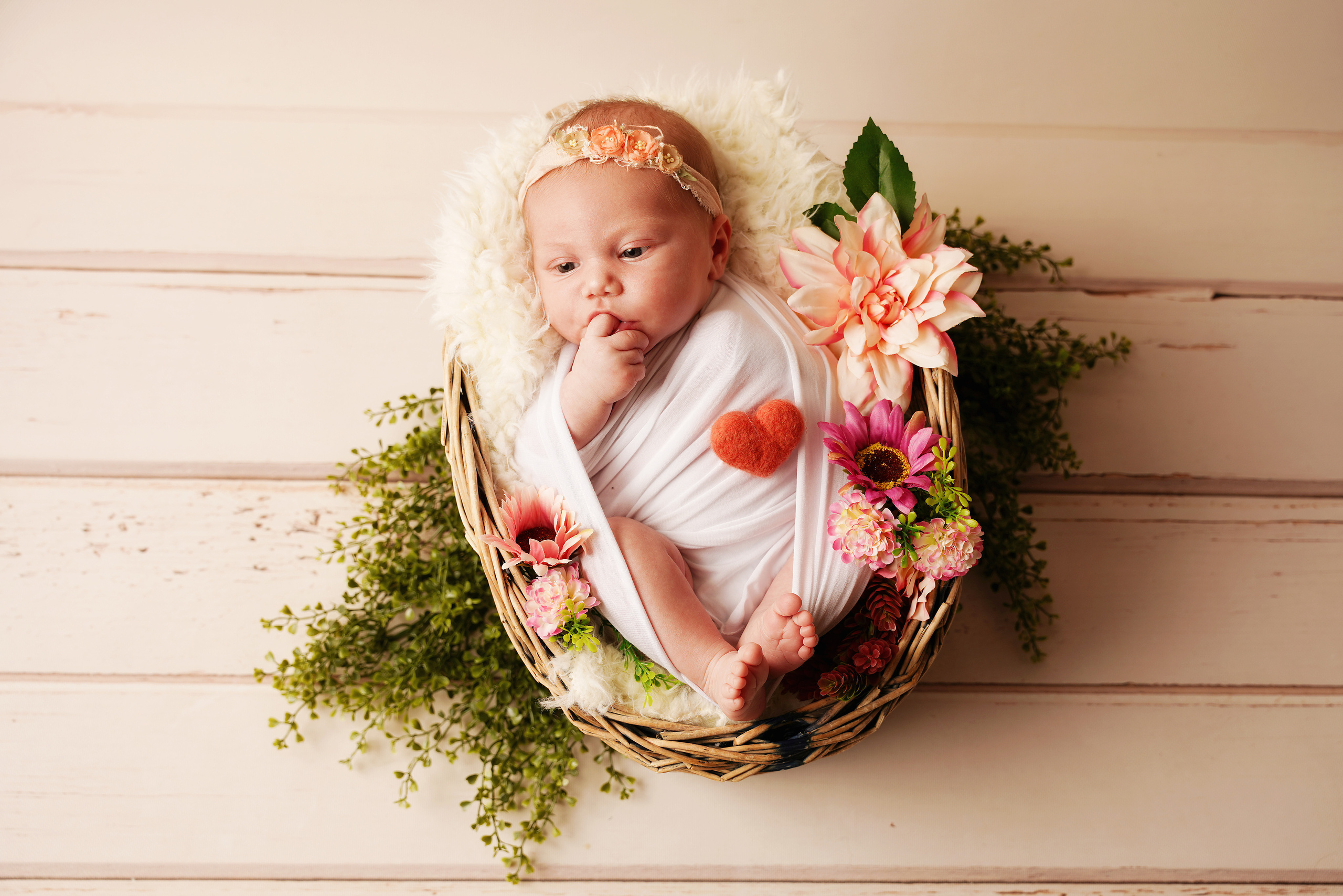Baby in Requisiten zwischen Blumen saugt an ihrem Finger
