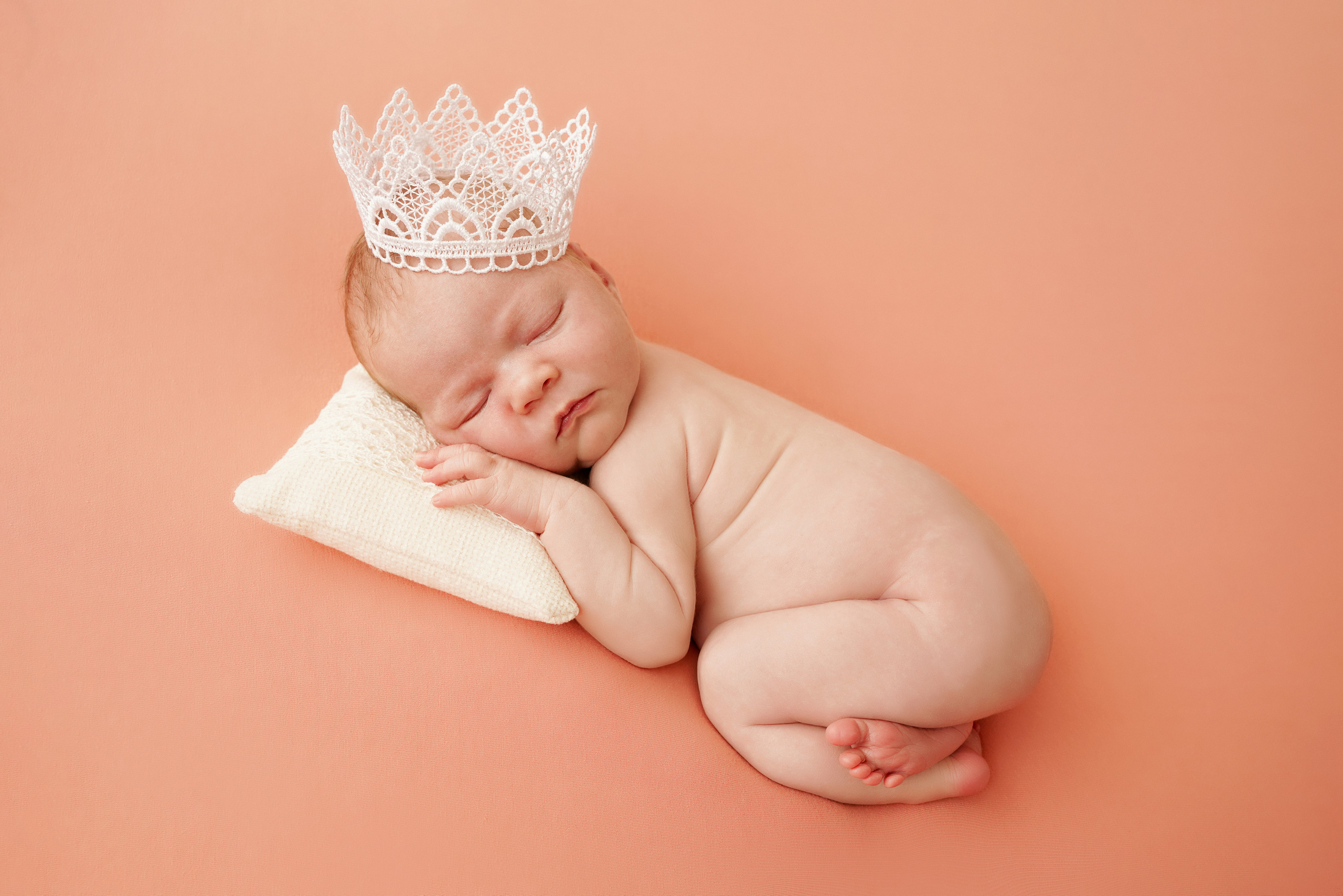 eine Krone auf dem Kopf eines in einer Glocke zusammengerollten Babys