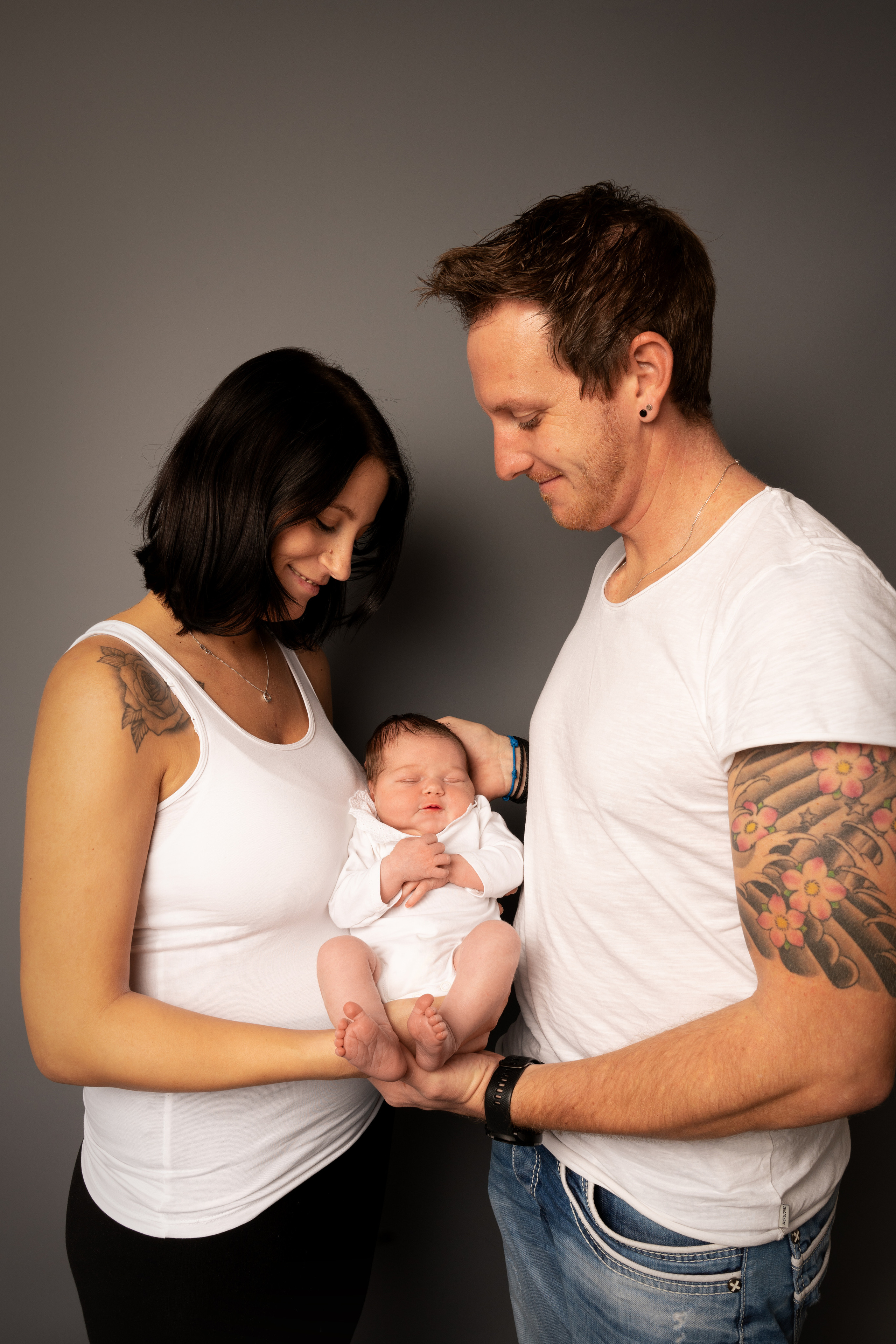 Eltern mit Tätowierungen auf den Armen mit einer neugeborenen Tochter