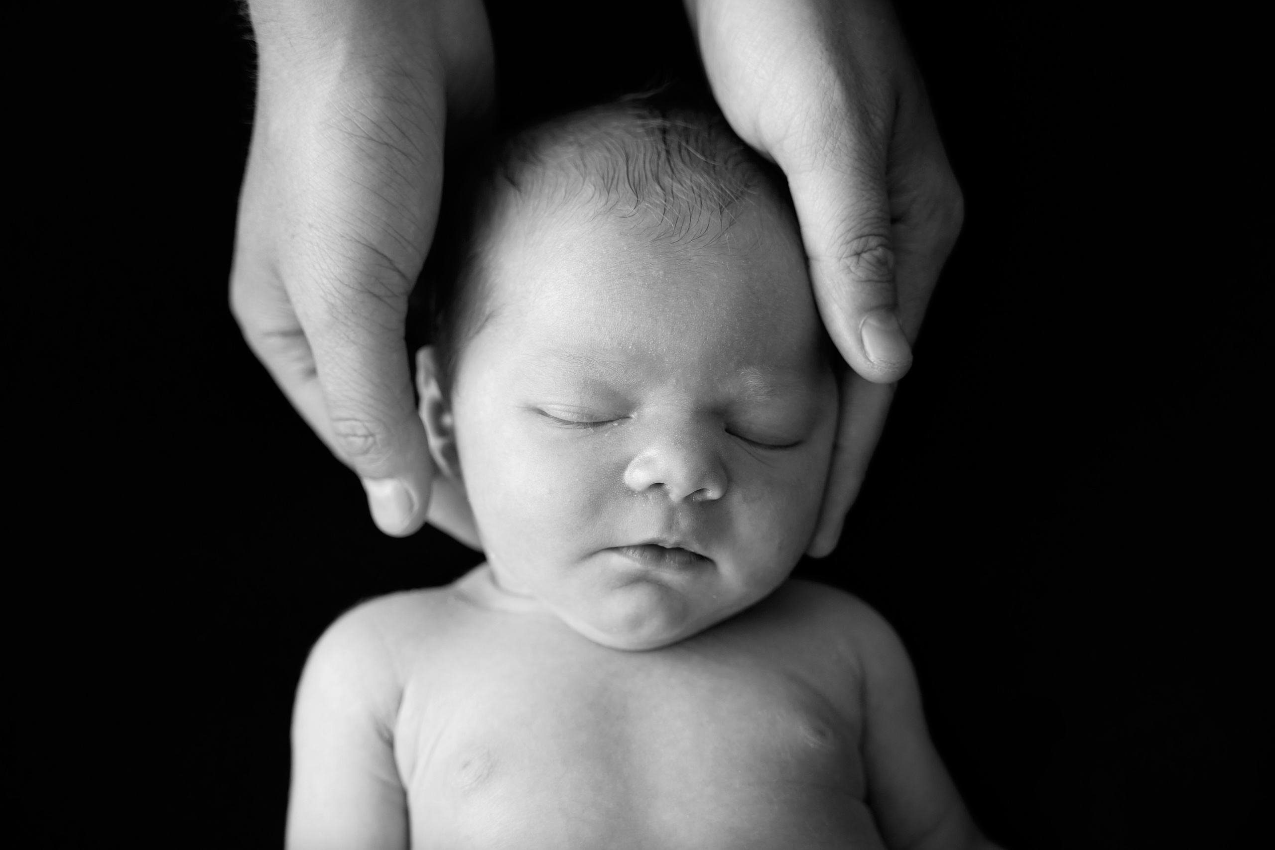 der kleine Kopf des Kindes liegt auf den Handflächen des Vaters