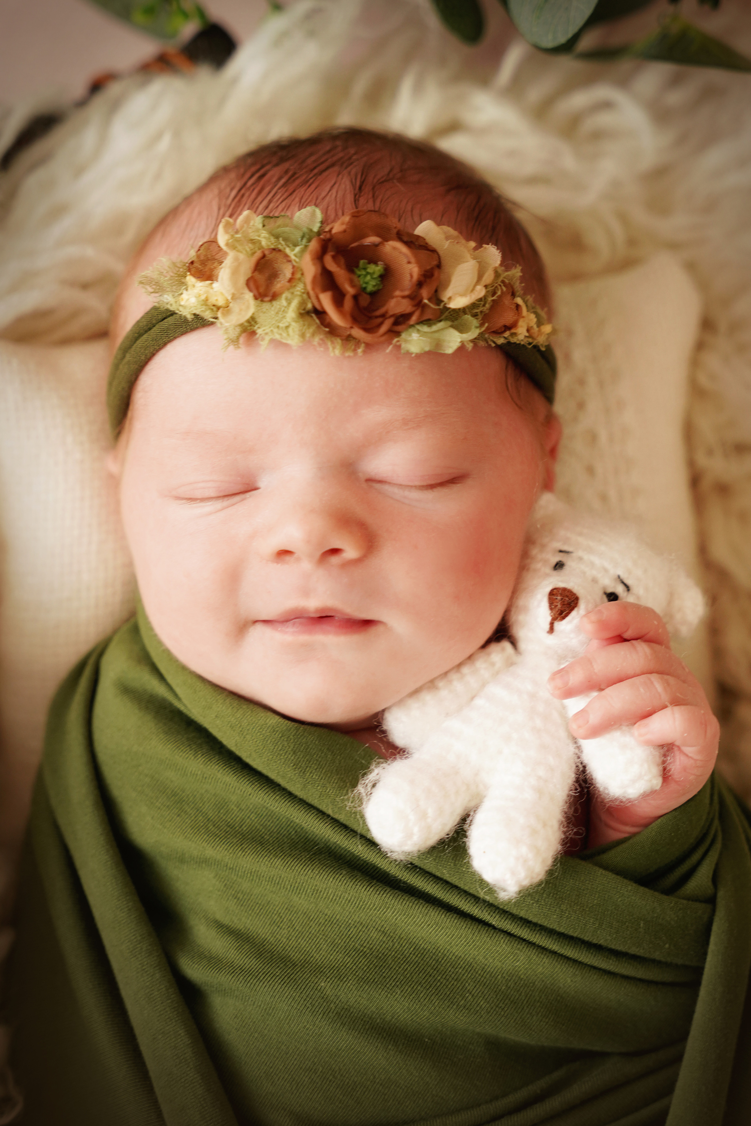Babymädchen umarmt  einen weißen gestrickten Bären mit einer Hand und lächelt