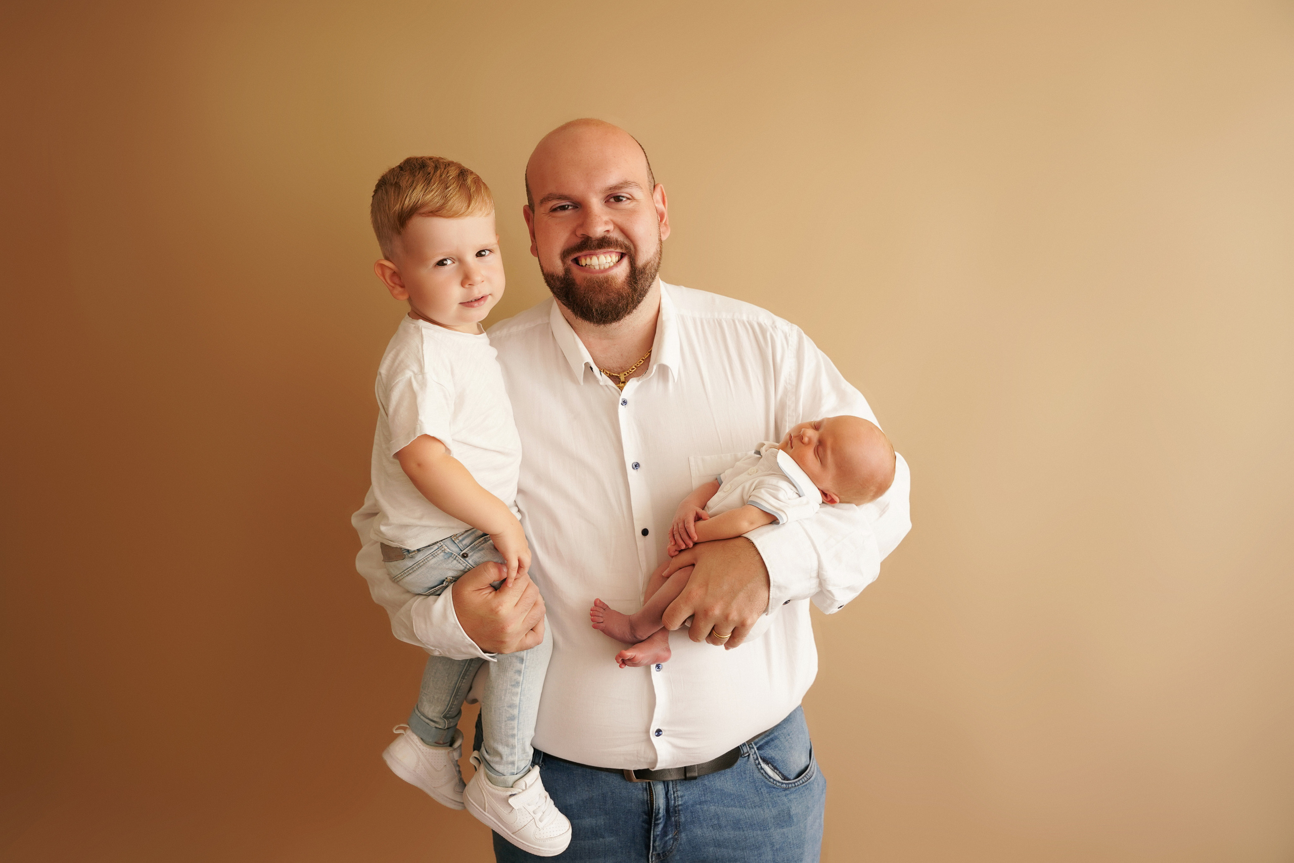 auf goldenem Hintergrund im Fotostudio hält ein Vater zwei Söhne in den Armen