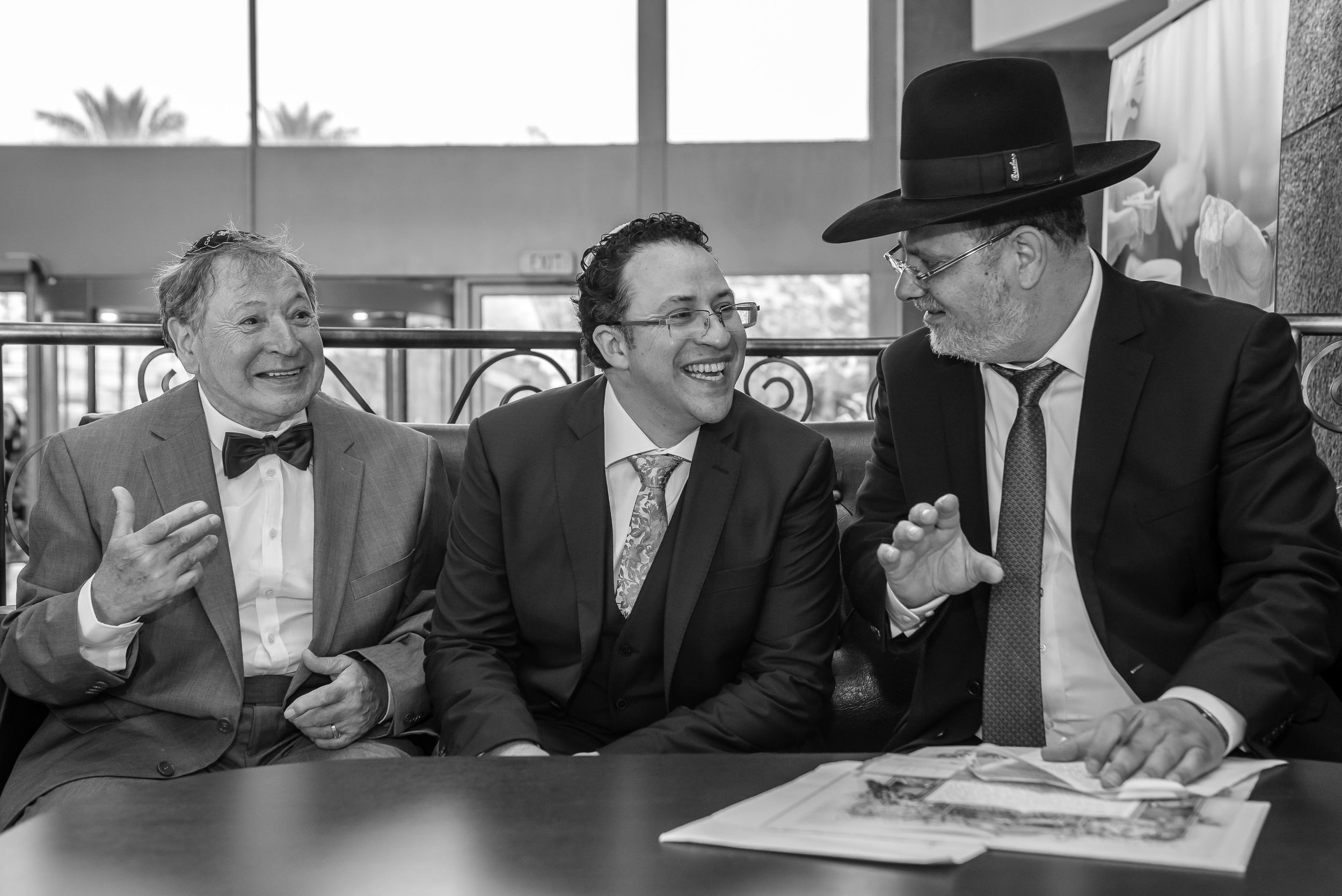 Black and white documentary wedding photography of a groom laughing during the traditional Ketubah signing ceremony with a rabbi in Israel