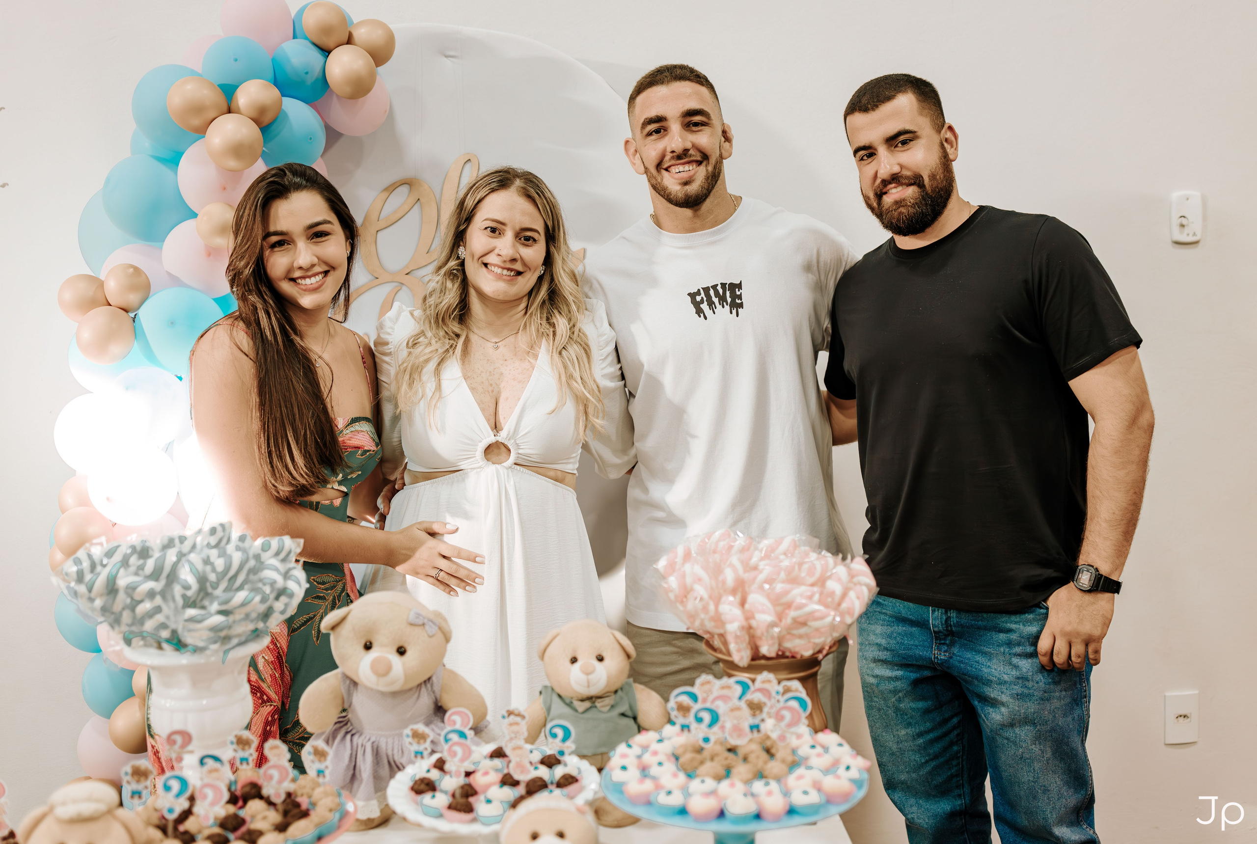 Quatro pessoas em pé ao lado da decoração com bolo e balões azuis.