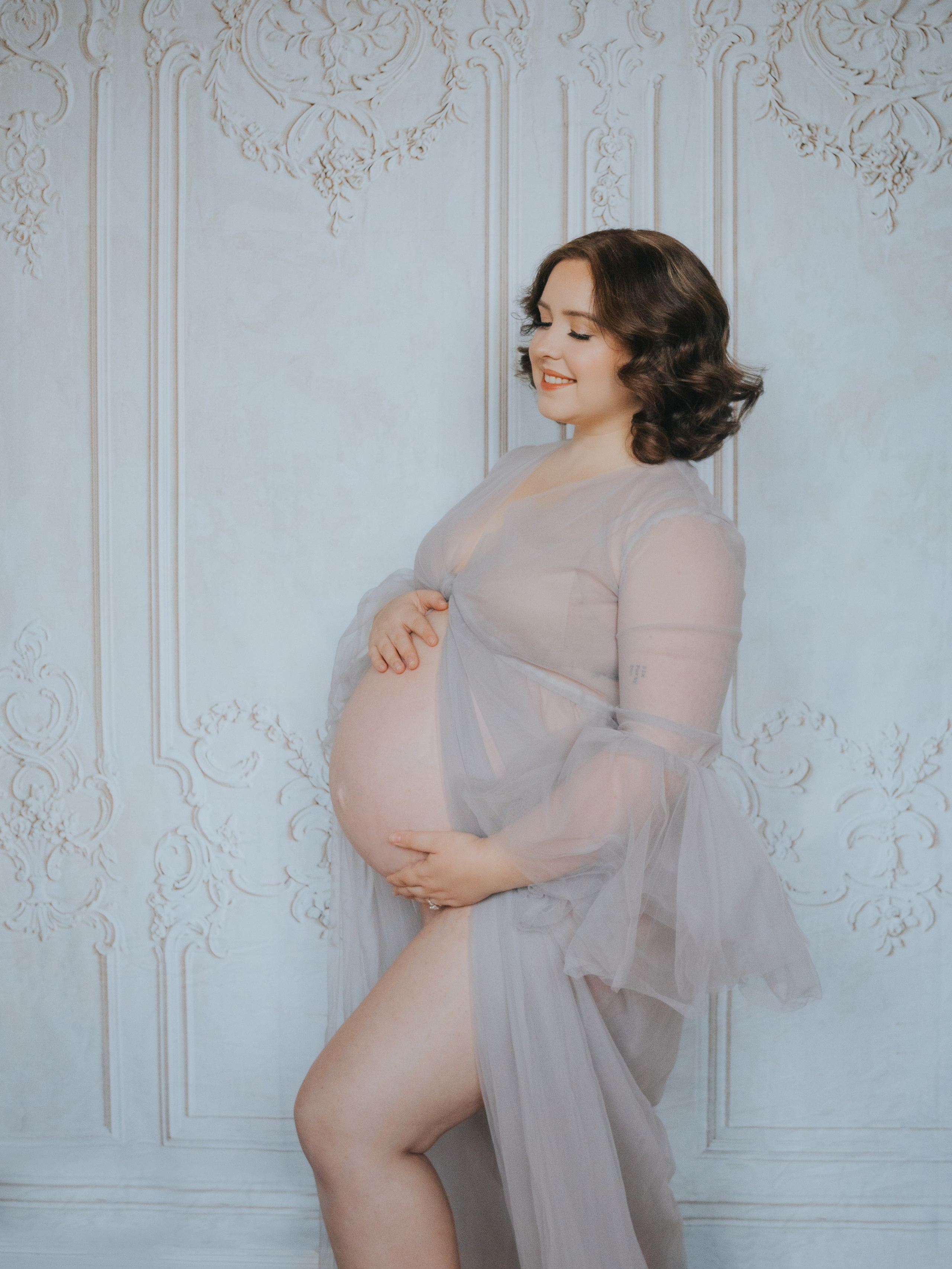 Pregnant woman in front of a wall with moldings.