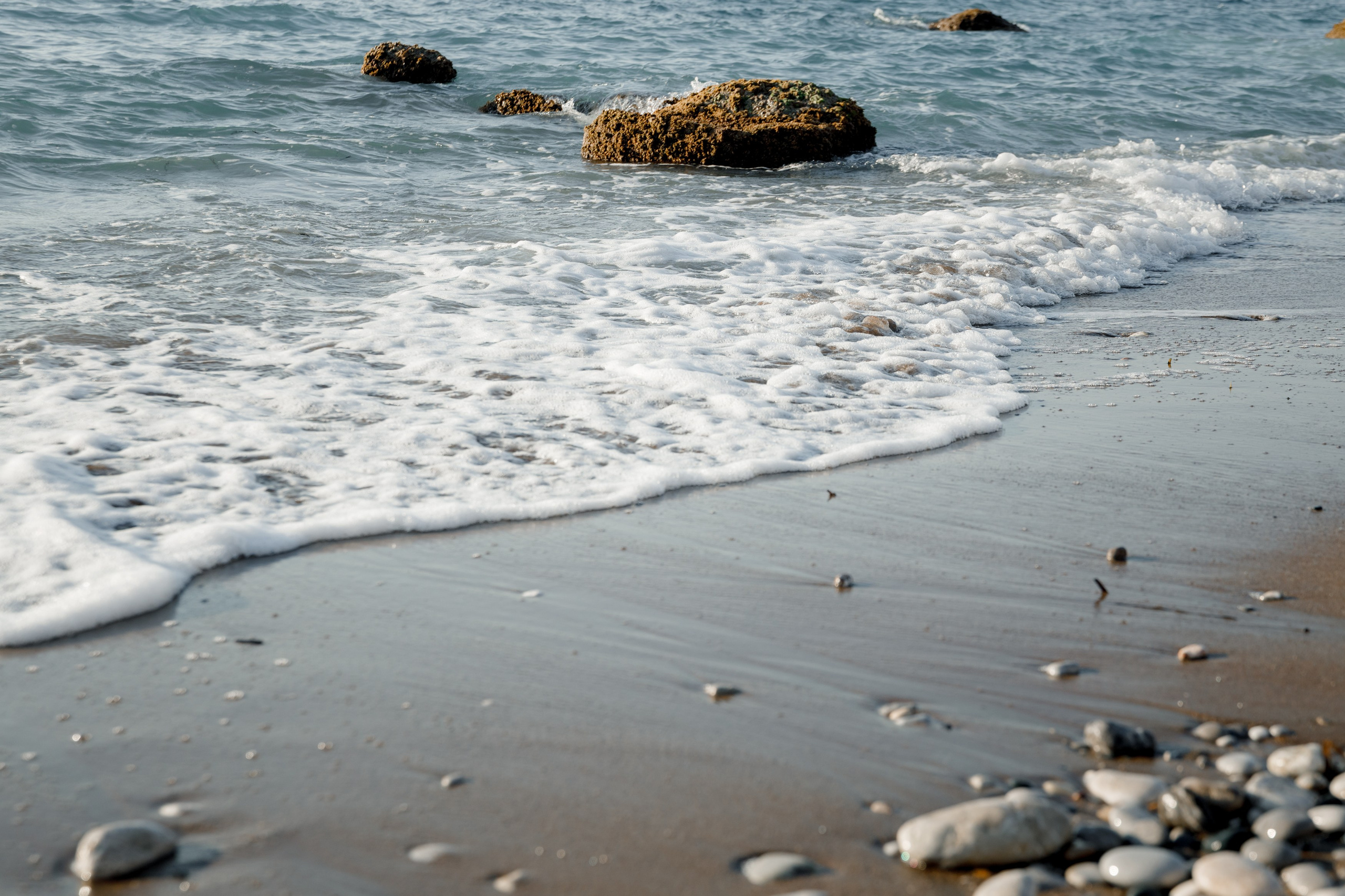 "Blick auf die charakteristischen Kalksteinfelsen am Strand von Kato Petres. Die von Wind und Wasser geformten Höhlungen in den Klippen bieten einen starken Kontrast zum klaren, türkisfarbenen Wasser und dem hellen Kieselstrand."