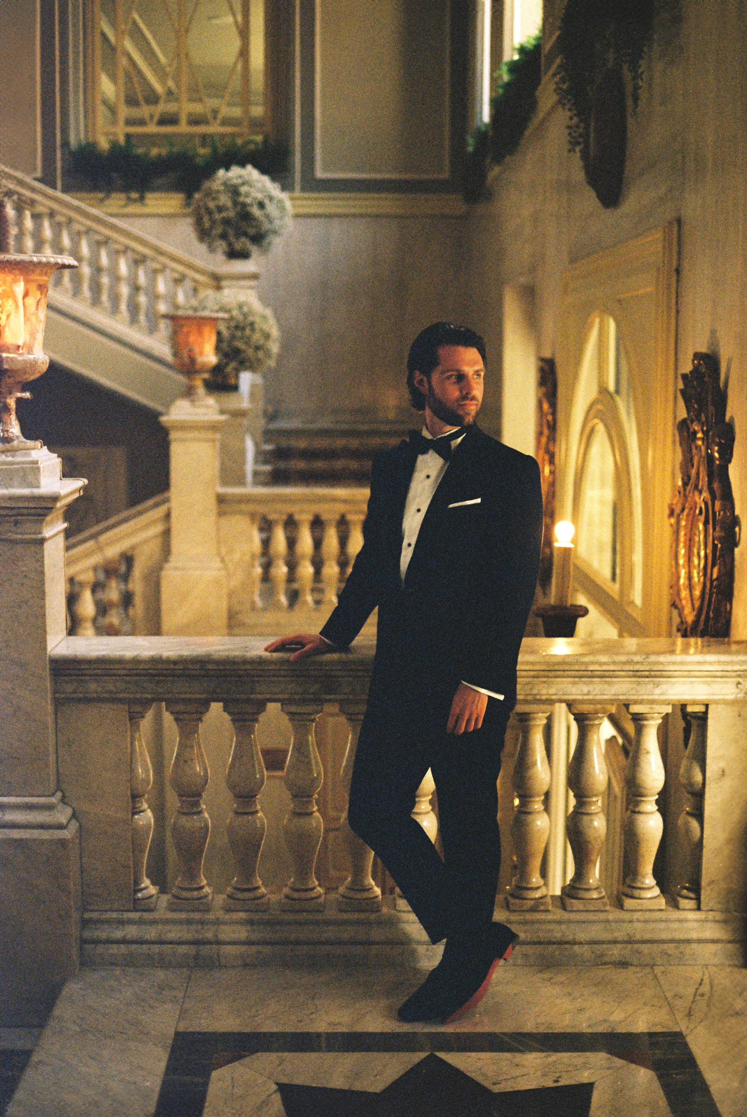 Elegant groom stands confidently in luxurious hall, embodying classic sophistication.