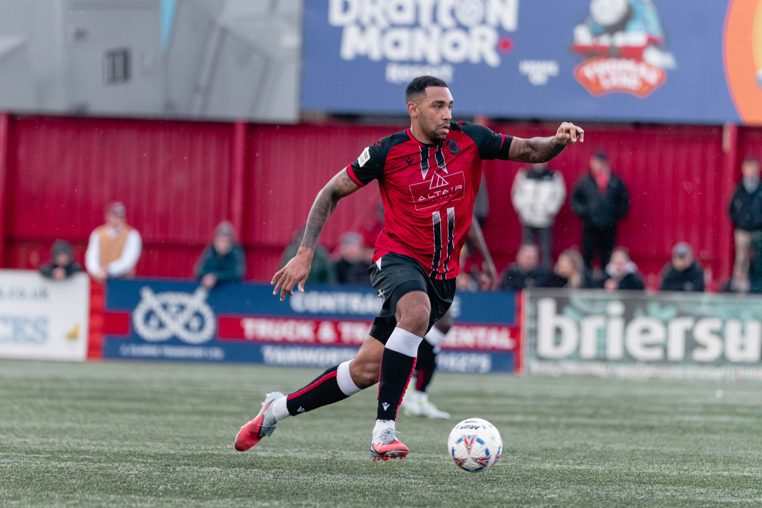 Jordan Cullinane-Liburd dribbles forward in Tamworth’s red-and-black kit with the ball at his feet during the National League match at The Lamb Ground.