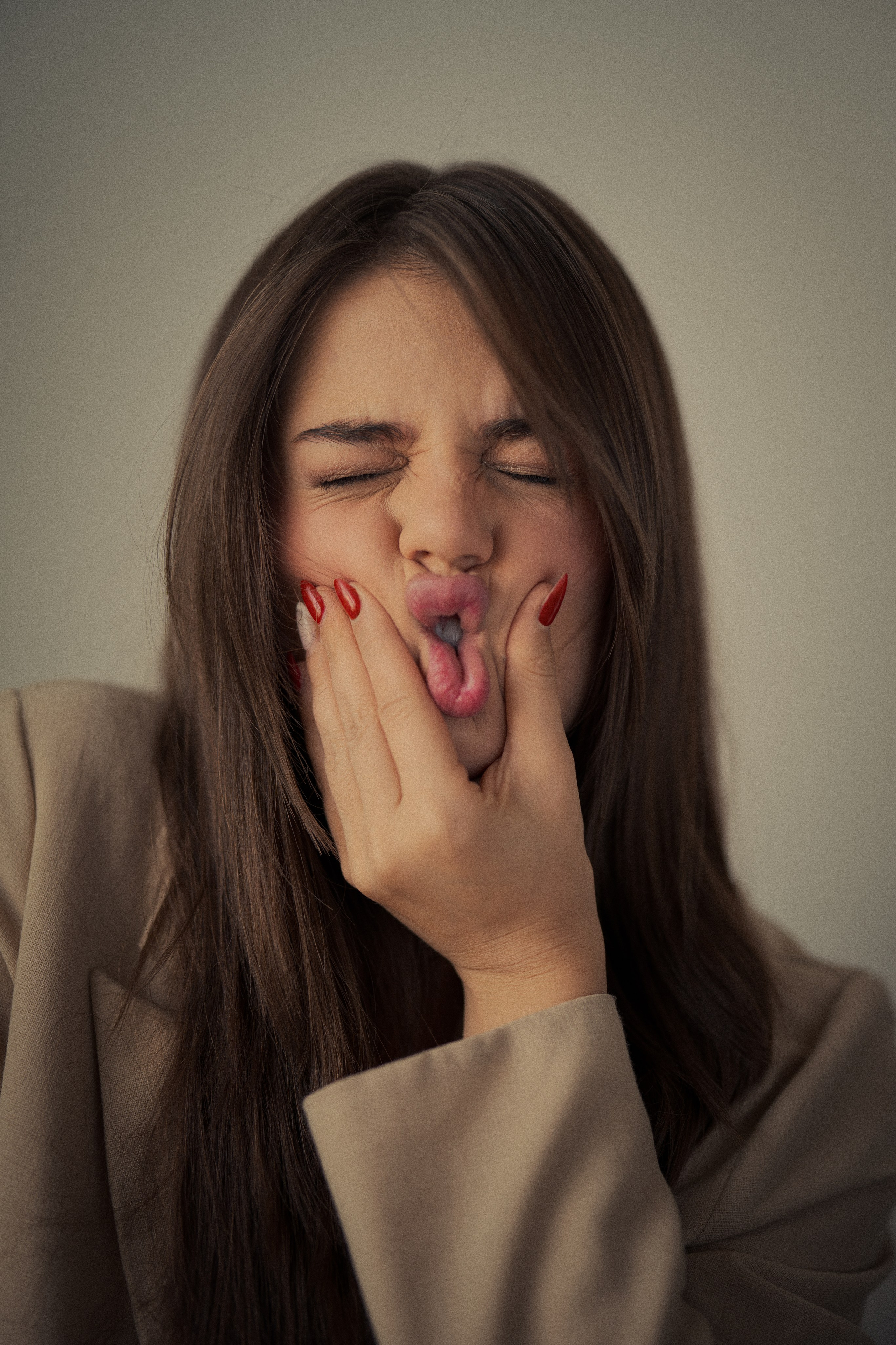 Playful female portrait photography by Mehran Hadad featuring Forouq Mohamadi making an expressive face with her hands against her cheeks in soft natural light.
