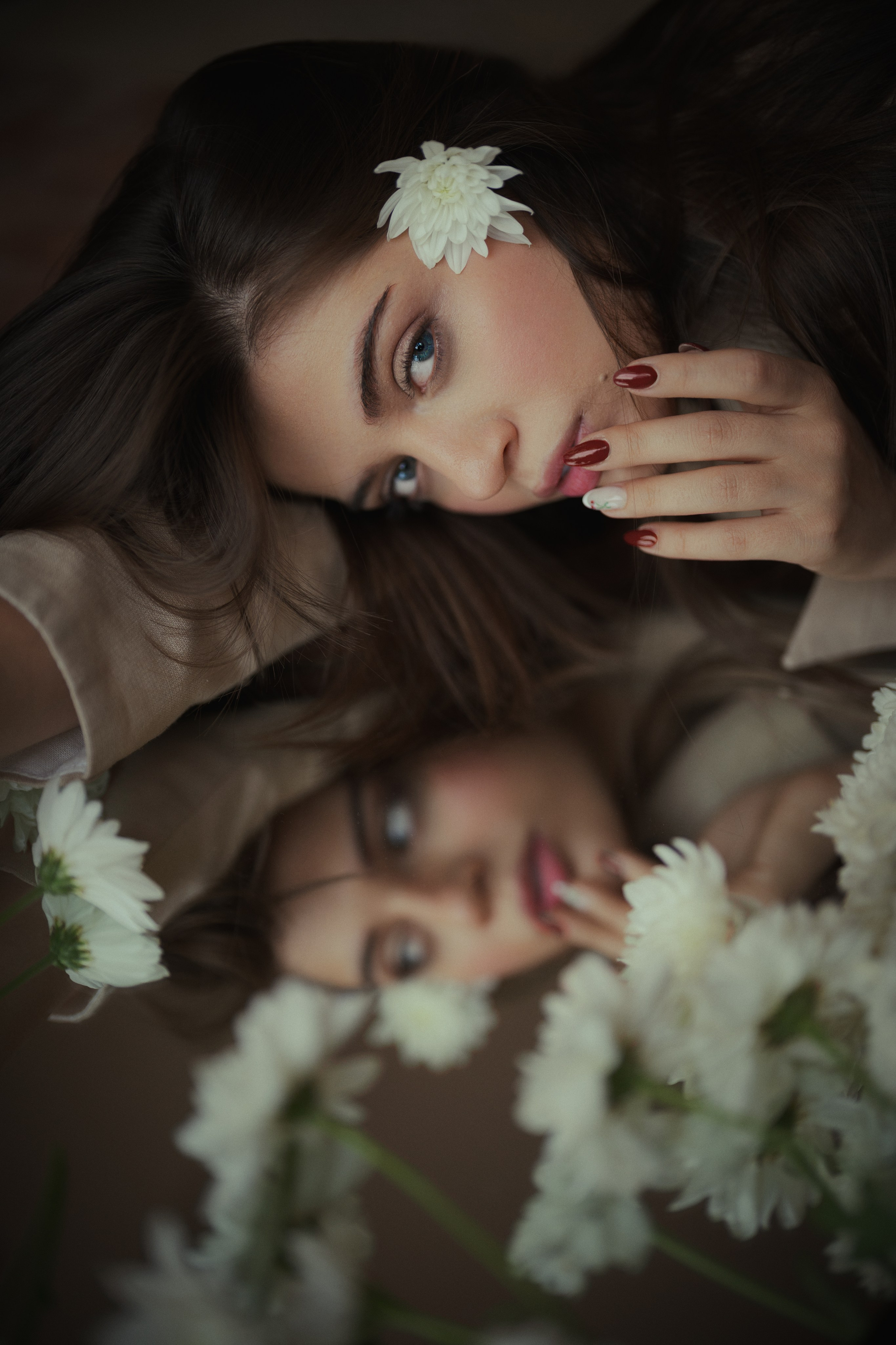 Close-up editorial portrait of a woman with a white flower in her hair and her reflection visible in the mirror, by Mehran Hadad.