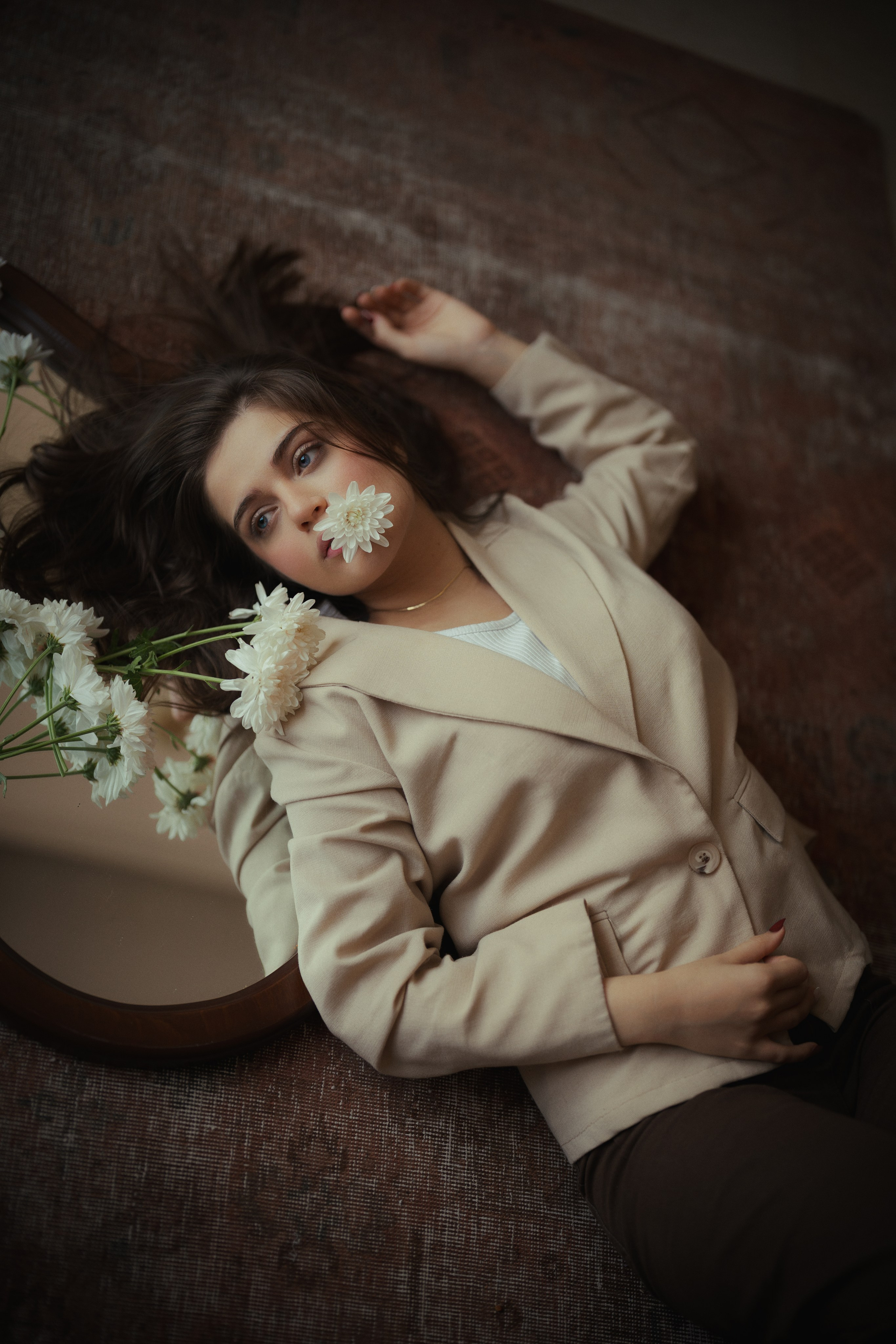 Cinematic portrait of a woman reclining beside a mirror with white flowers, featuring warm tones and soft natural light by Mehran Hadad.