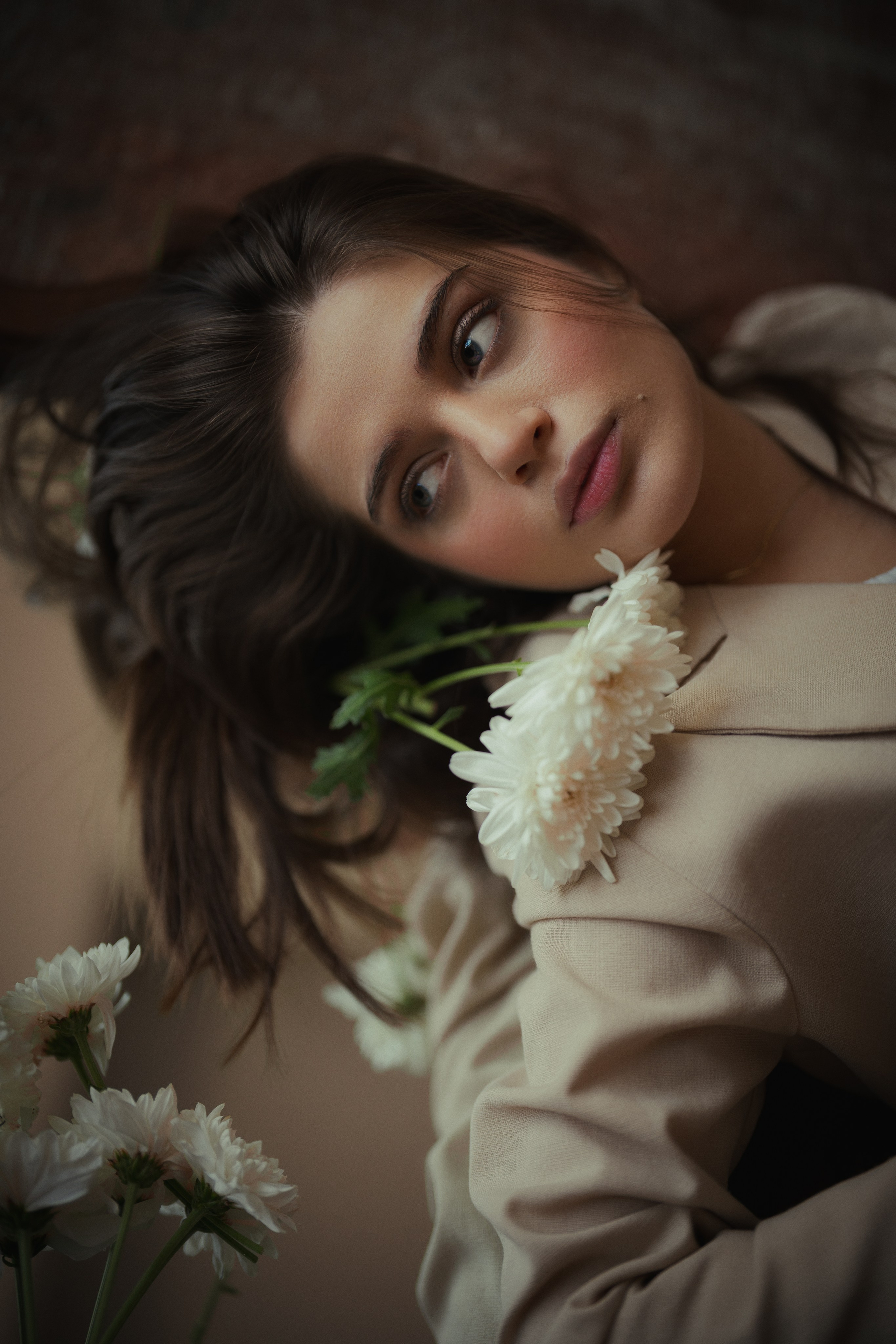 Soft editorial portrait of a woman with white flowers against a warm neutral background, photographed by Mehran Hadad.