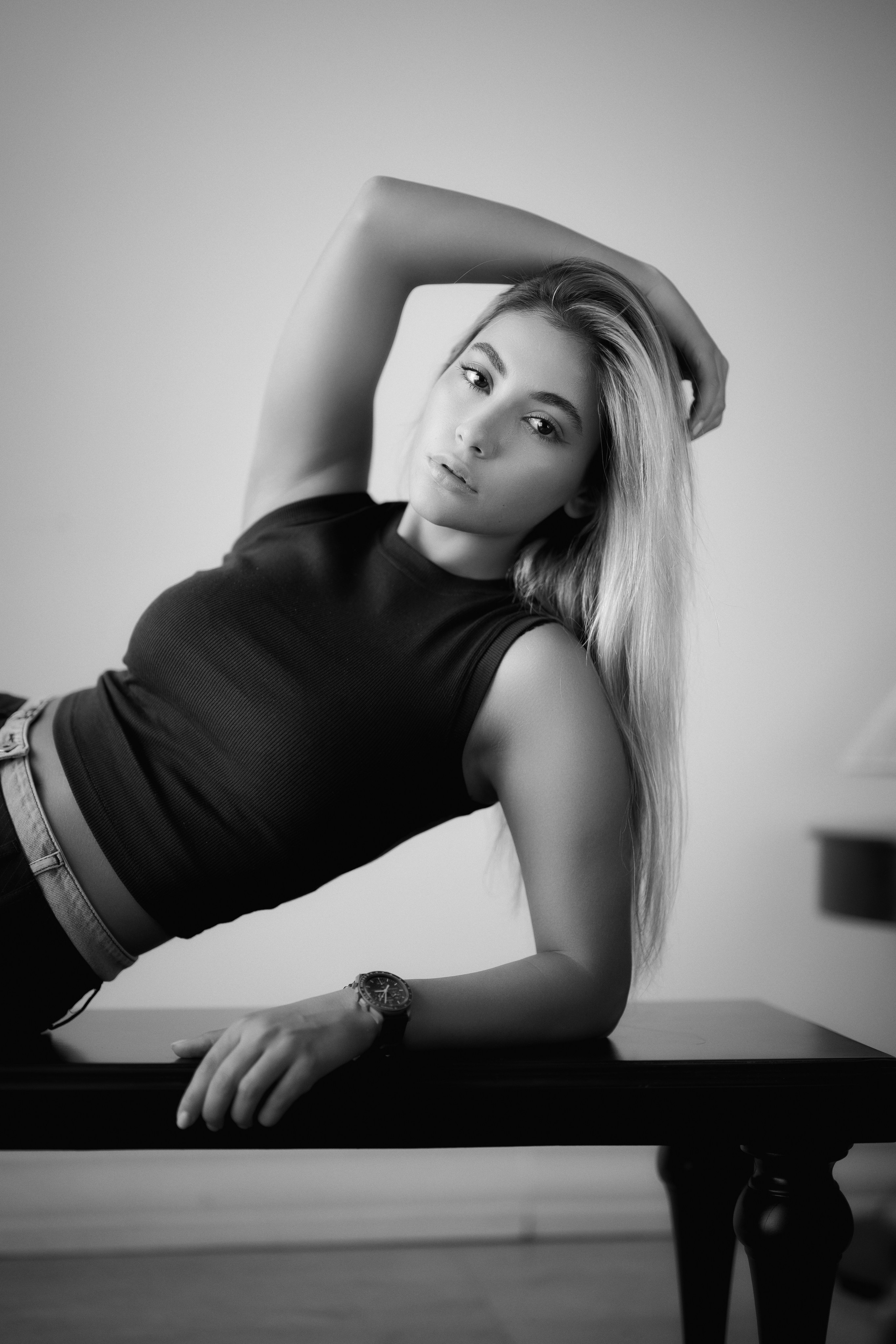 Black and white fashion portrait of a woman reclining on a table and looking at the camera, featuring elegant posing and soft natural light by Mehran Hadad.