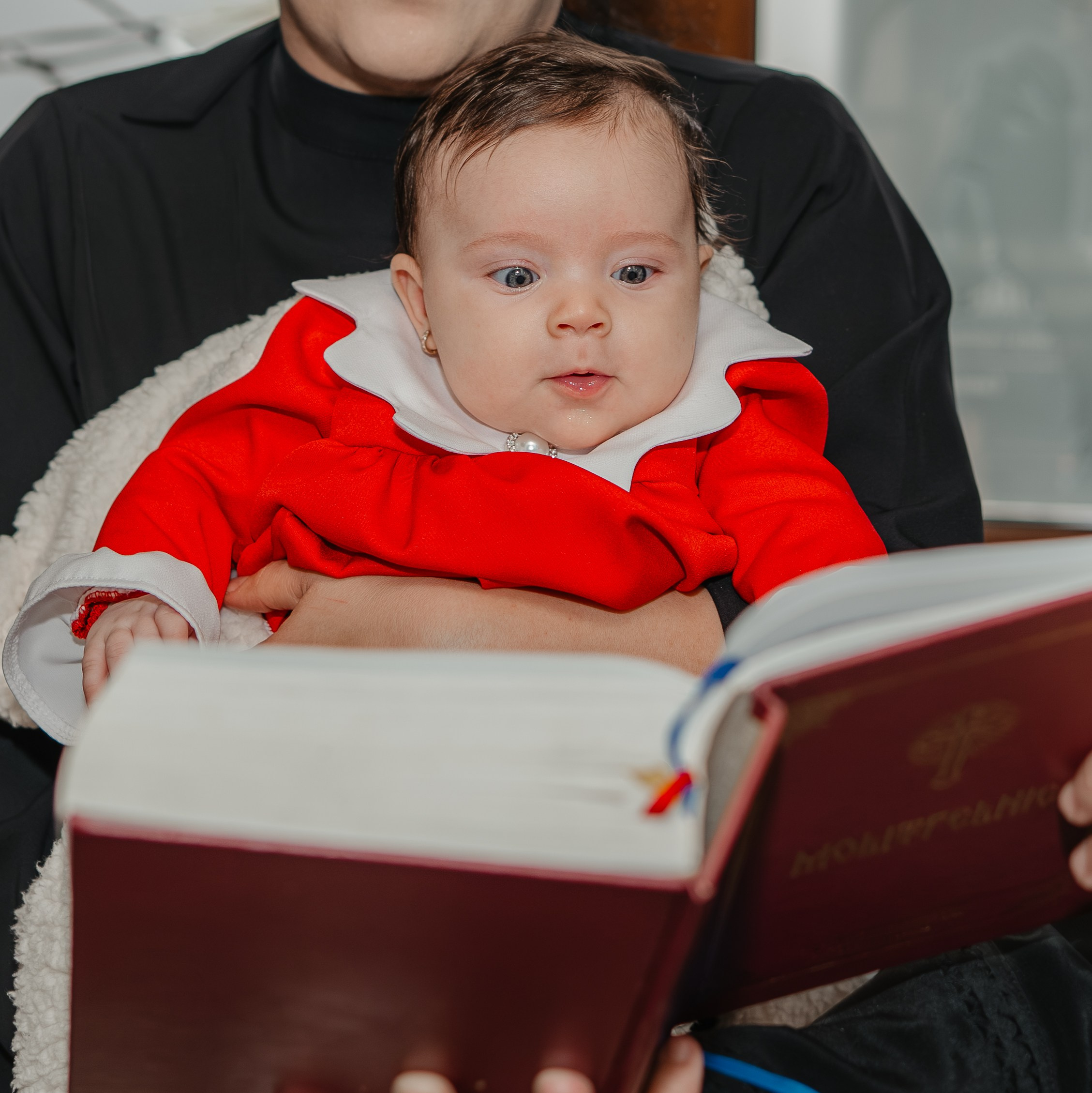 Detaliu extrem de aproape: chipul fascinat al pruncului Eveline Maria, izolat complet în timp ce privește profund și curios către paginile unei cărți sfinte la botez. Fotografie intimă care captează magia privirii inocente.