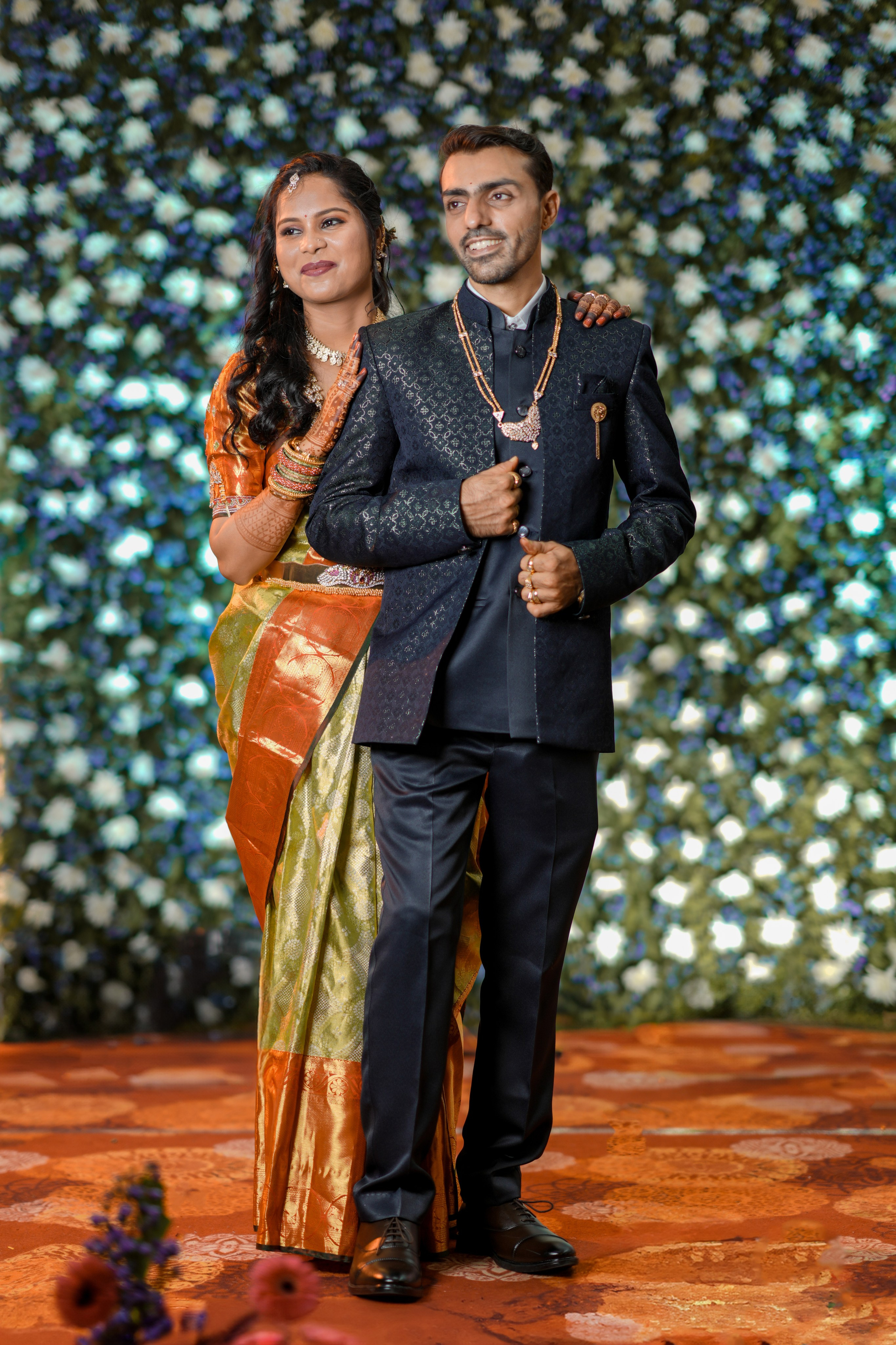 professional photograph of a newly married South Indian couple posing in wedding attire against a floral backdrop in Malleshwaram, Bengaluru
