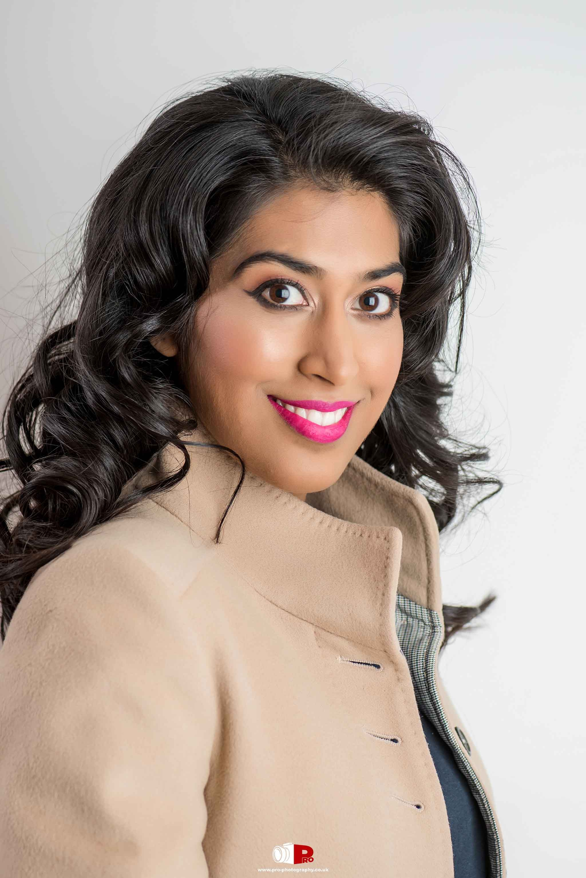 Close-up portrait of a cheerful woman in a beige coat with bold pink lipstick, ideal for beauty and fashion photography.