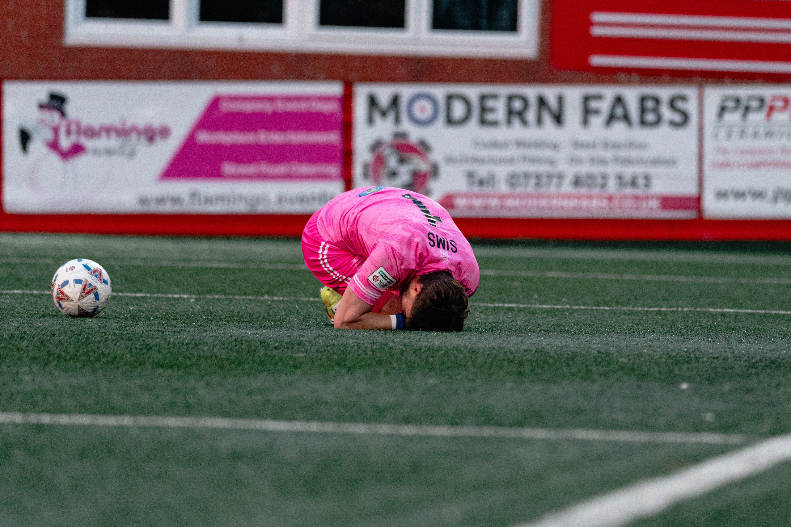 Sutton United goalkeeper Jack Sims lies on the pitch with the ball nearby during a stoppage in play.