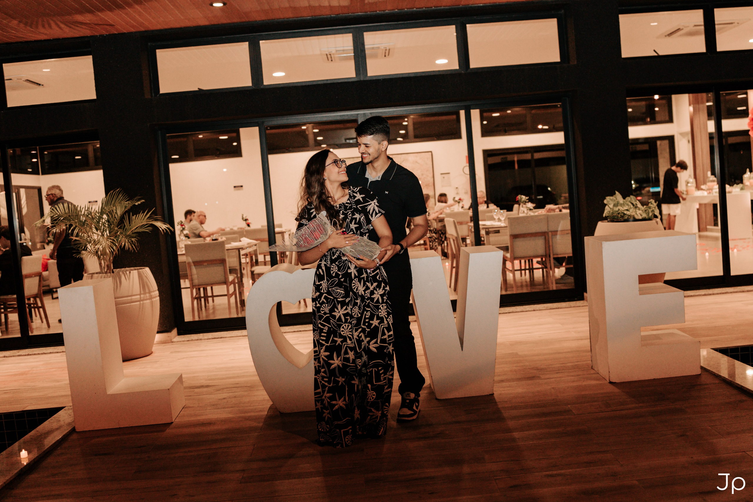 Casal posando em frente à palavra “LOVE” iluminada.