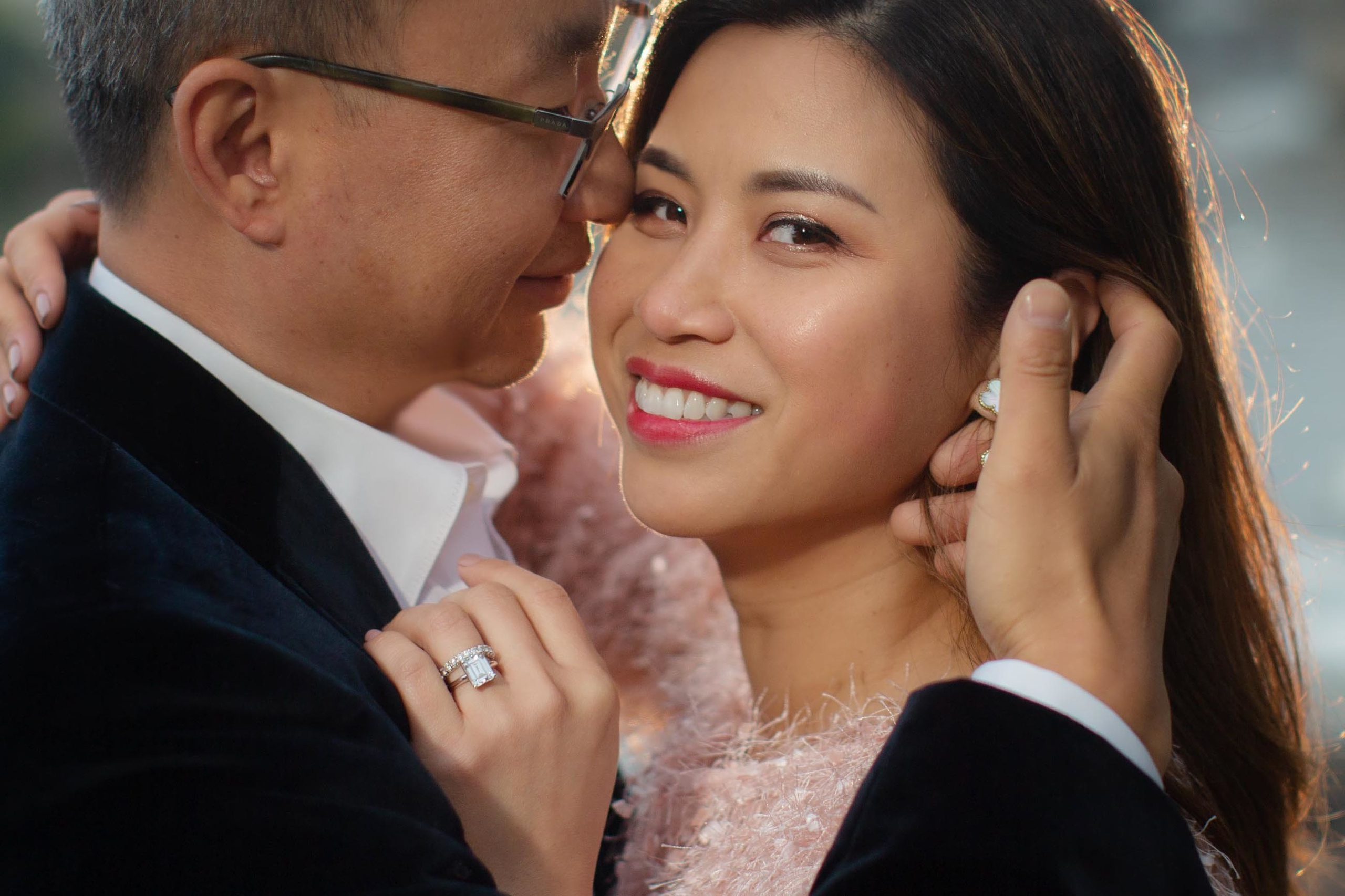 Close-up portait of a beautiful, elegant Asian woman being lovingly caressed by her partner as her large diamand ring is seen