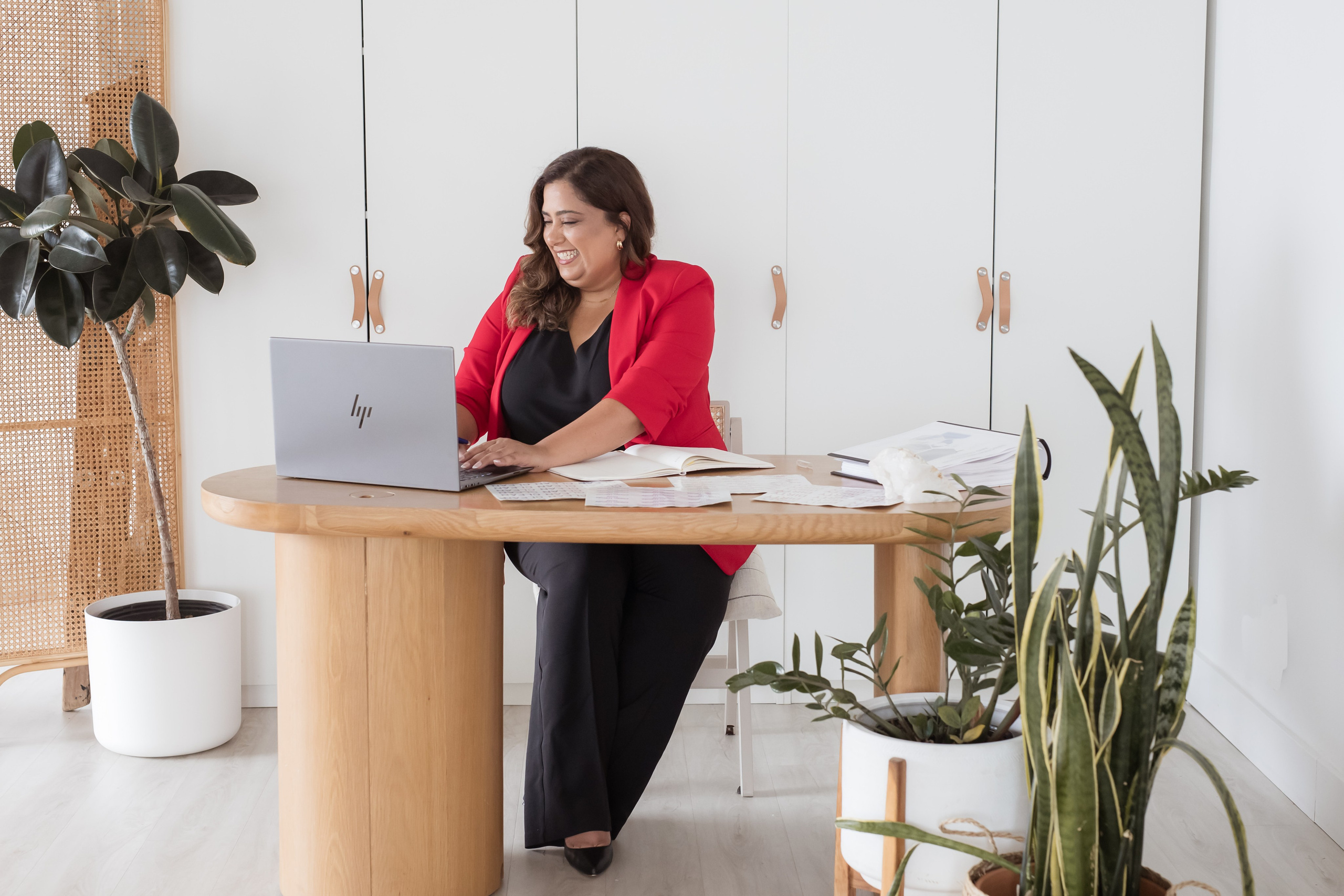 women in red blazer working at a desk on a computer 