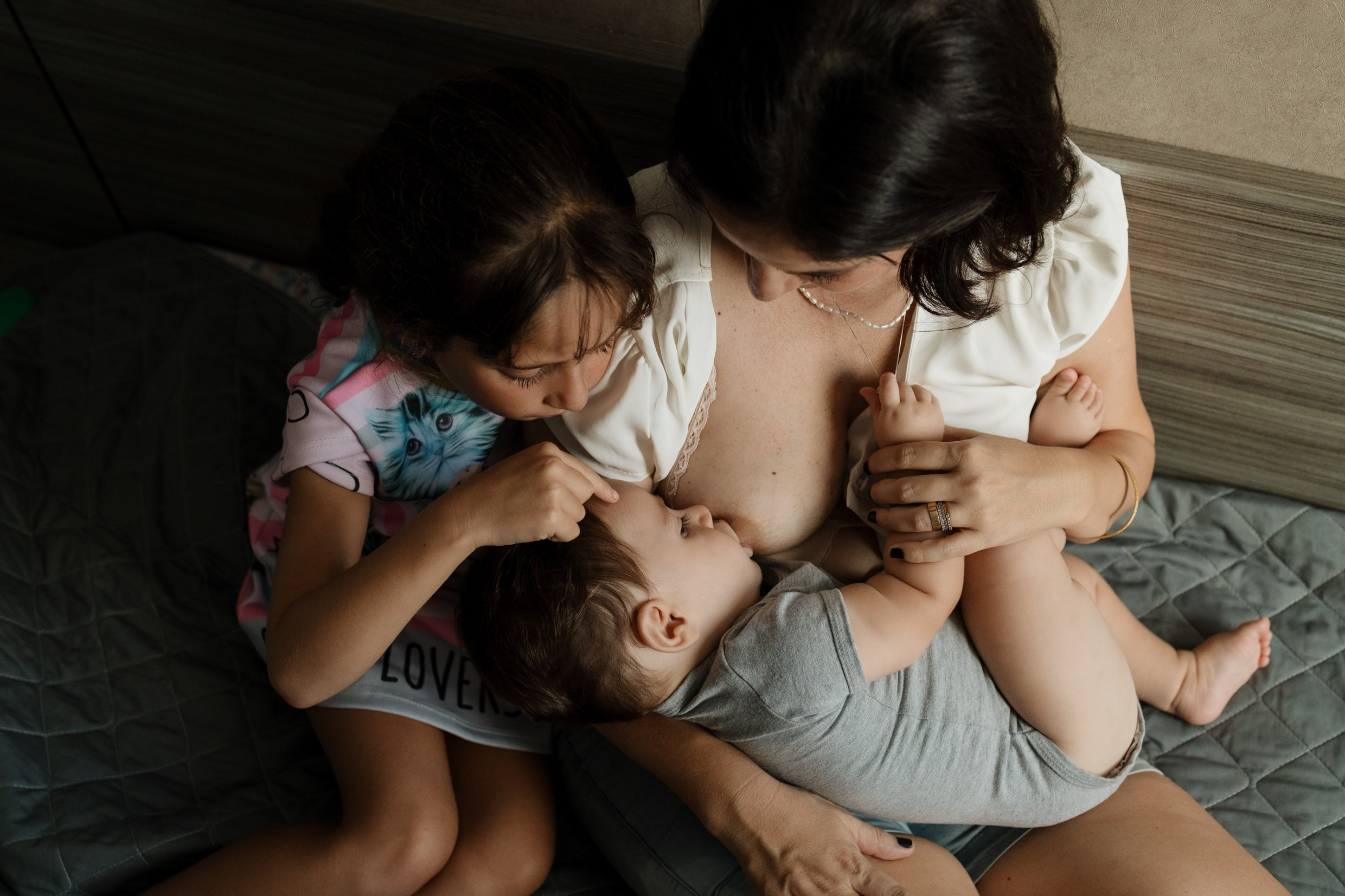 Mãe amamentando em momento intimista com irmã mais velha interagindo
