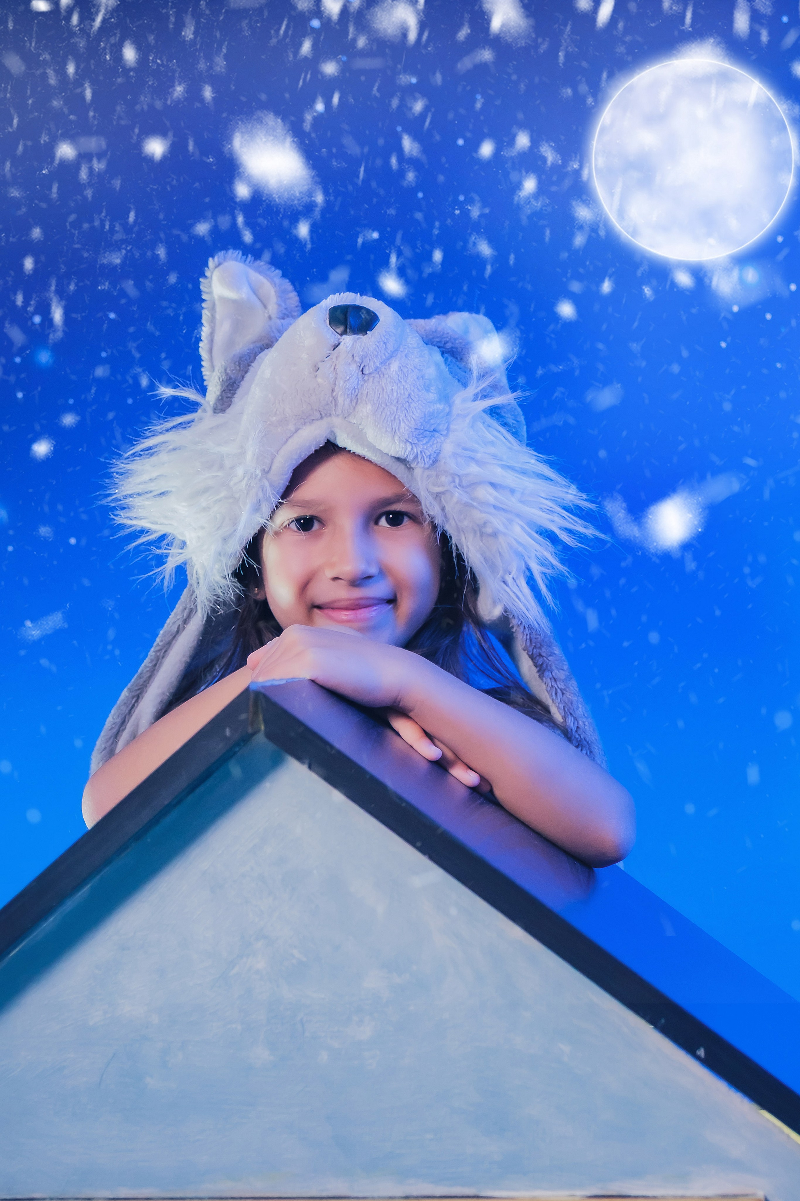 niña con gorro de lobo asomada al tejado de una casita nevada bajo la luna llena y los copos cayendo