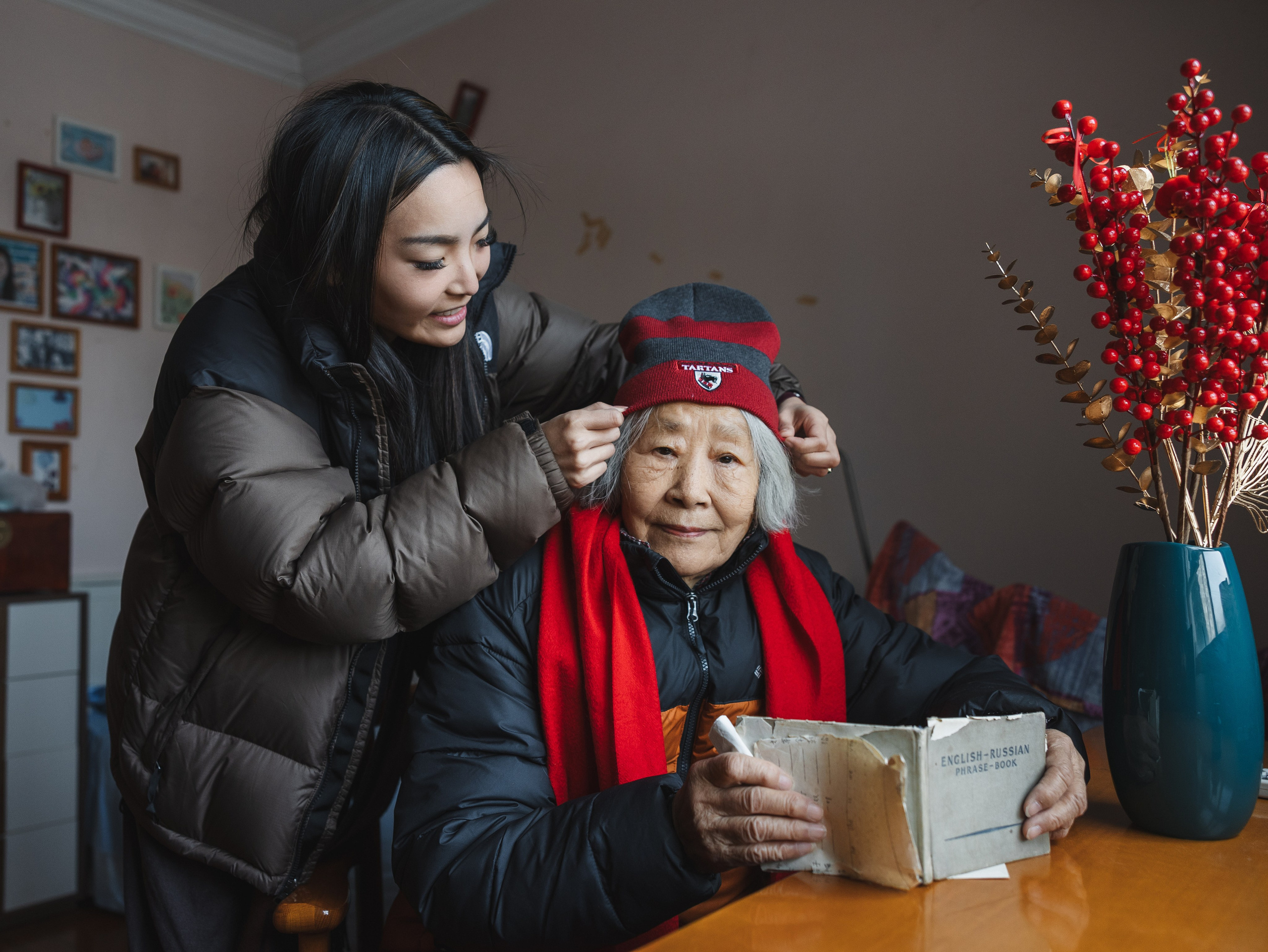 The granddaughter is helping her 90-year-old grandmother put on a hat.
