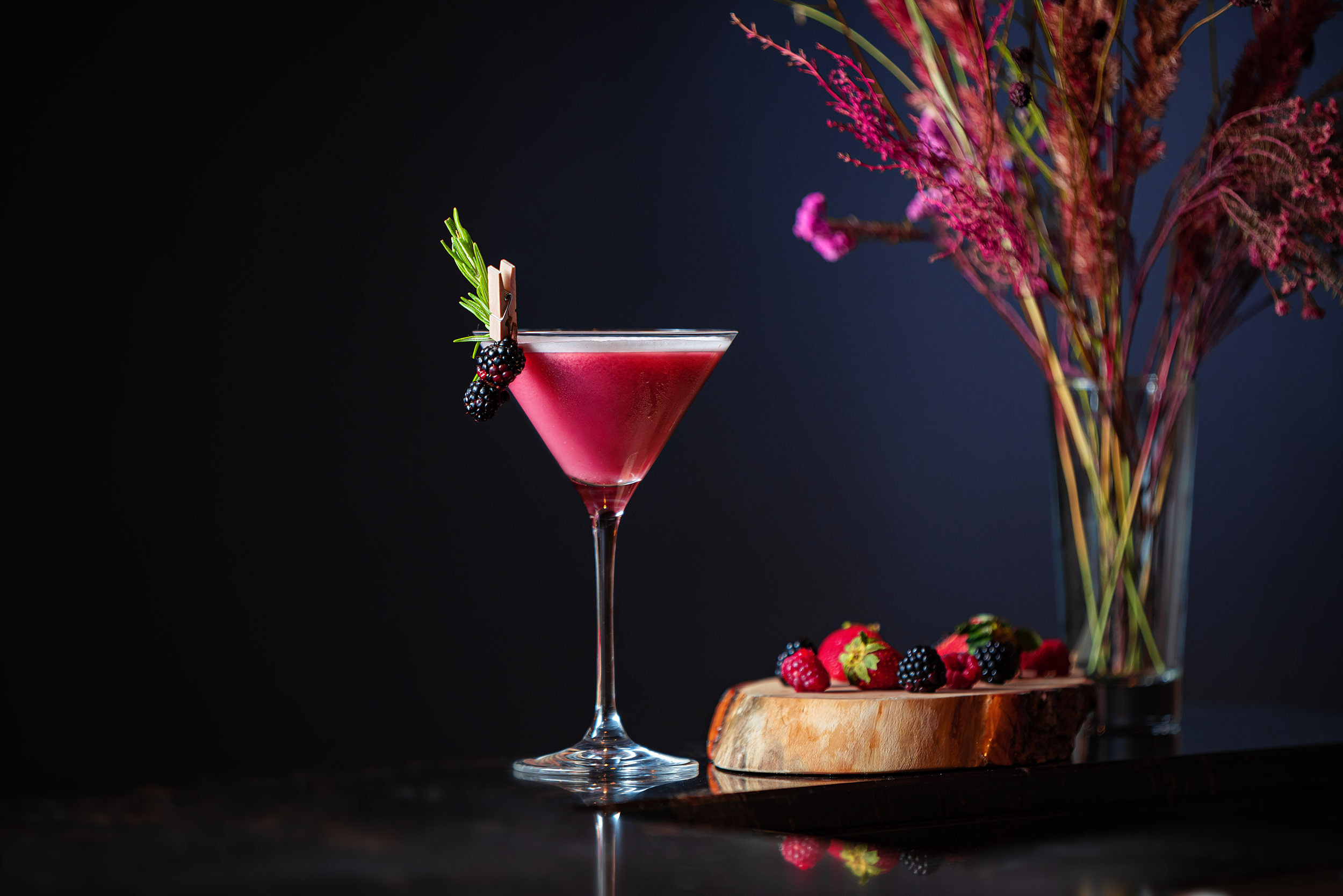 Red cocktail garnished with blackberries and herbs