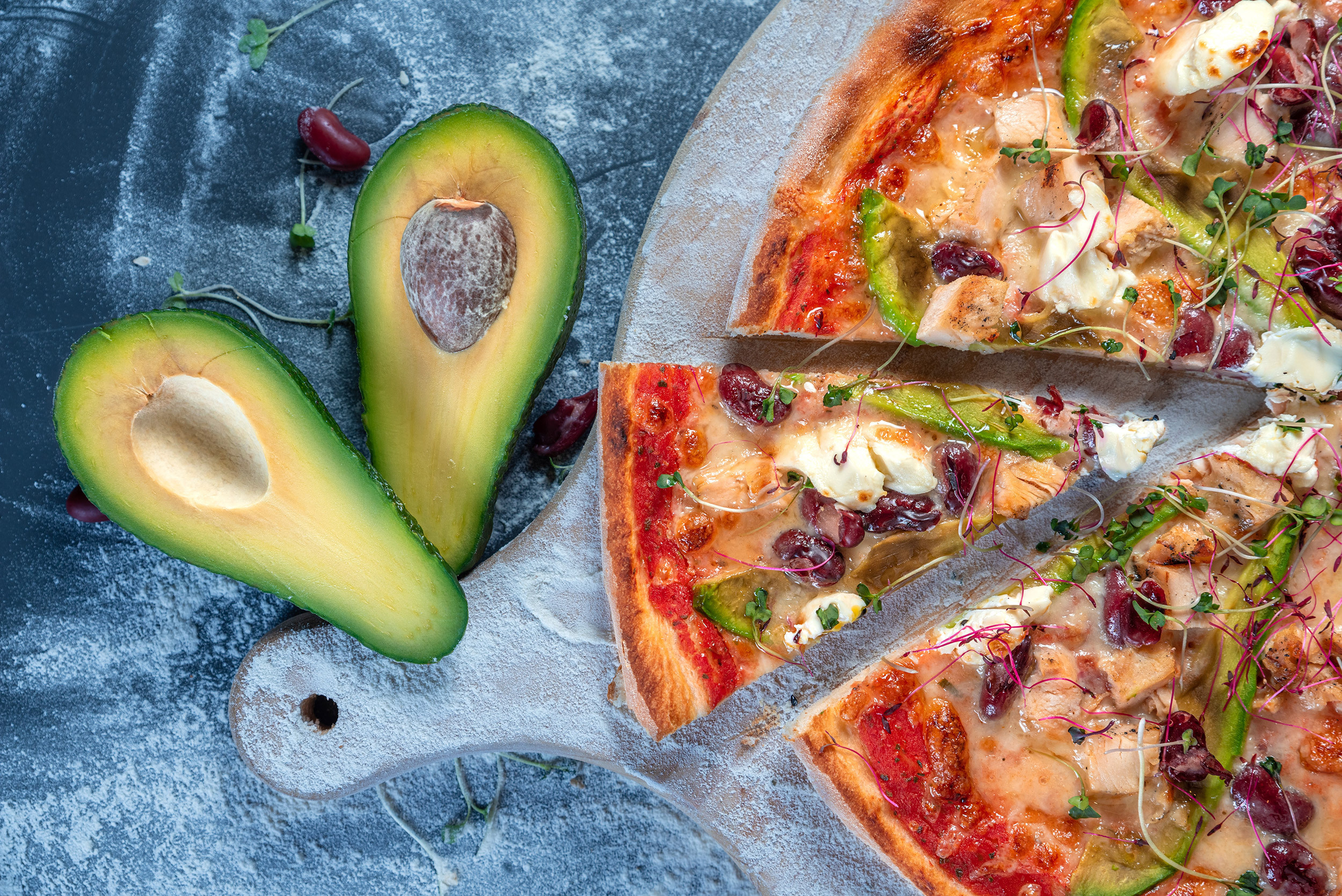Sliced avocado and vegetable pizza served on a wooden board