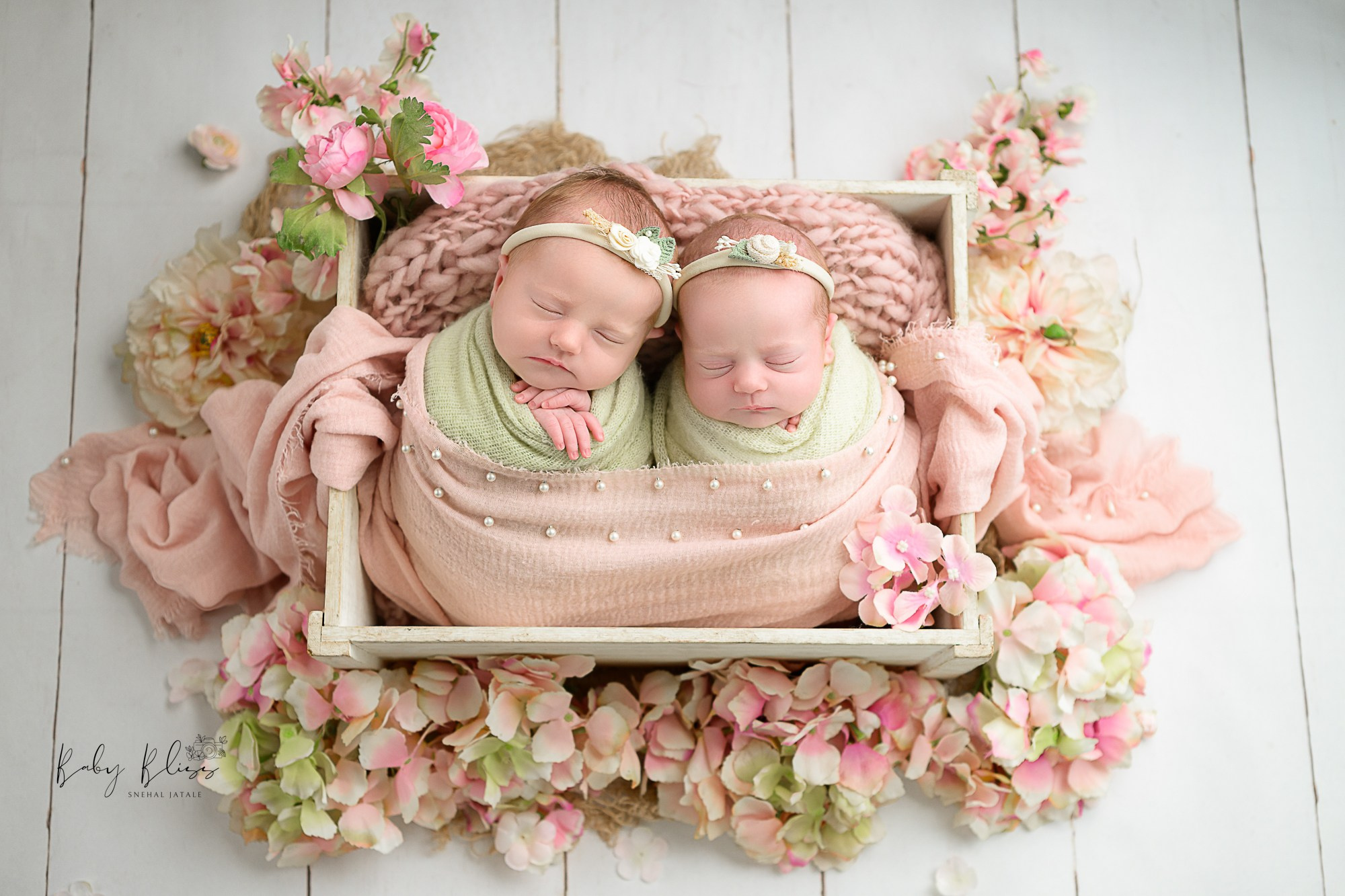 twins newborn baby girls are together in basket with pinkish and mint colour floral arrangement.