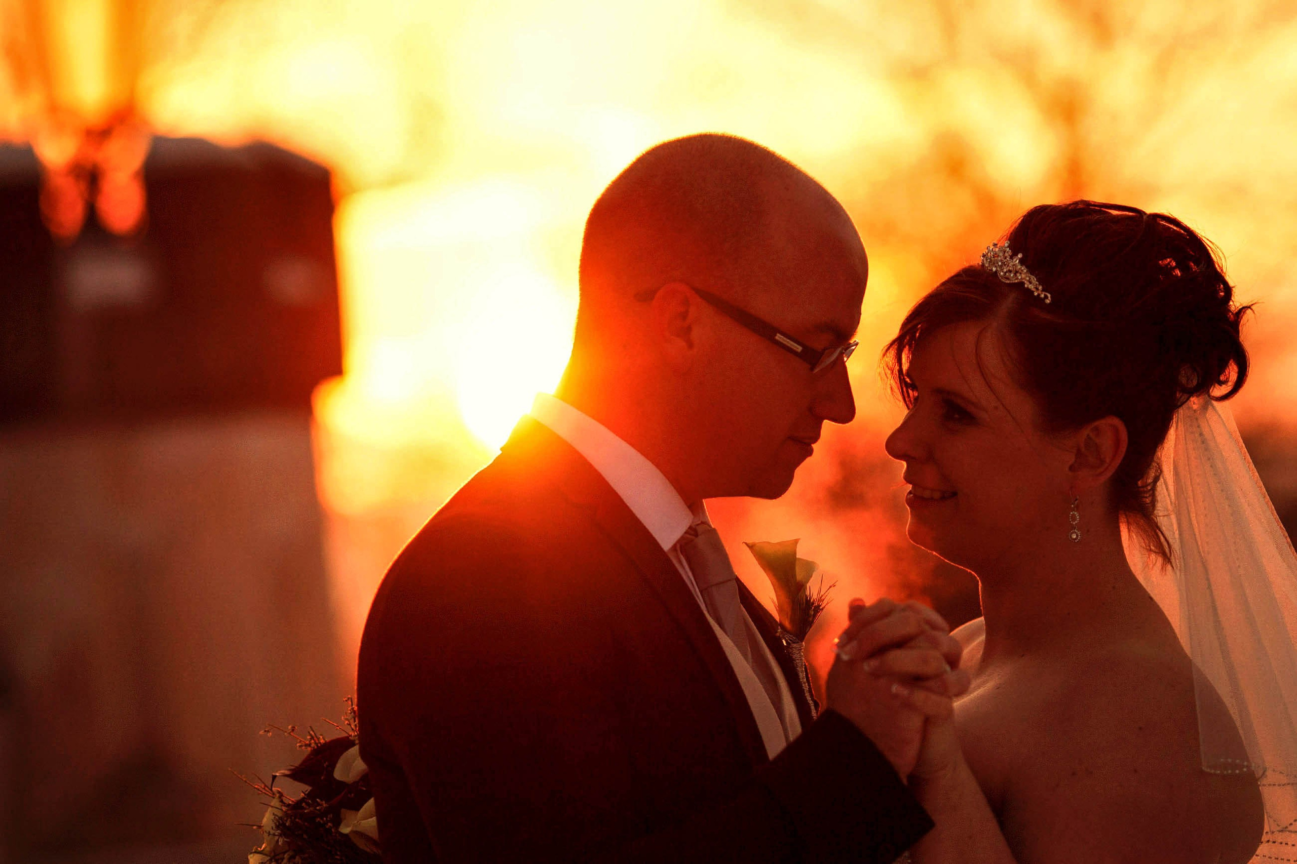 A bride and groom embrace as the freezing temperatures create a mist from their bodies warmth as they embrace in the winter landscape.