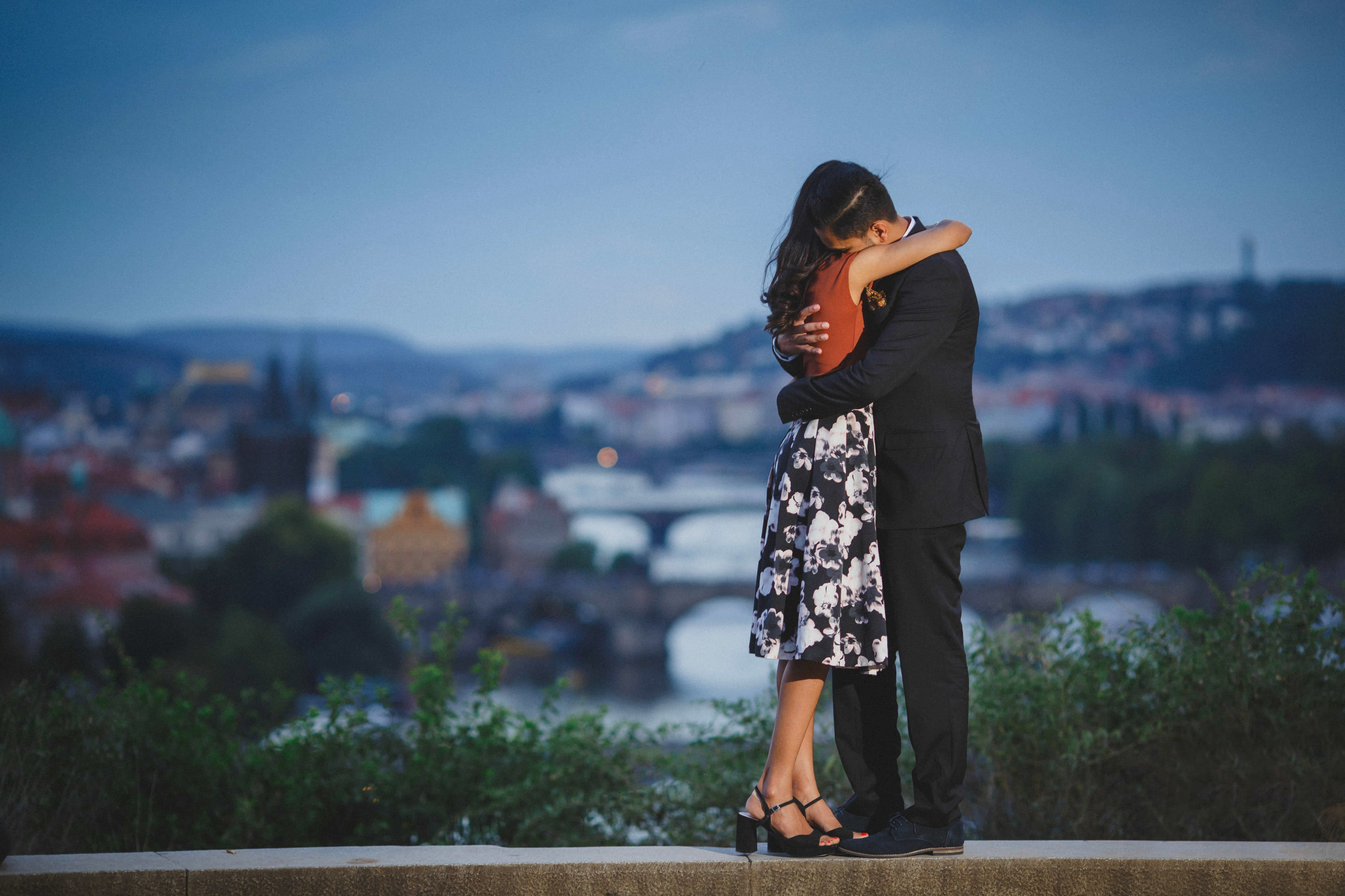 Indian couple sharing close embrace at Letná overlook high above Prague during blue hour.