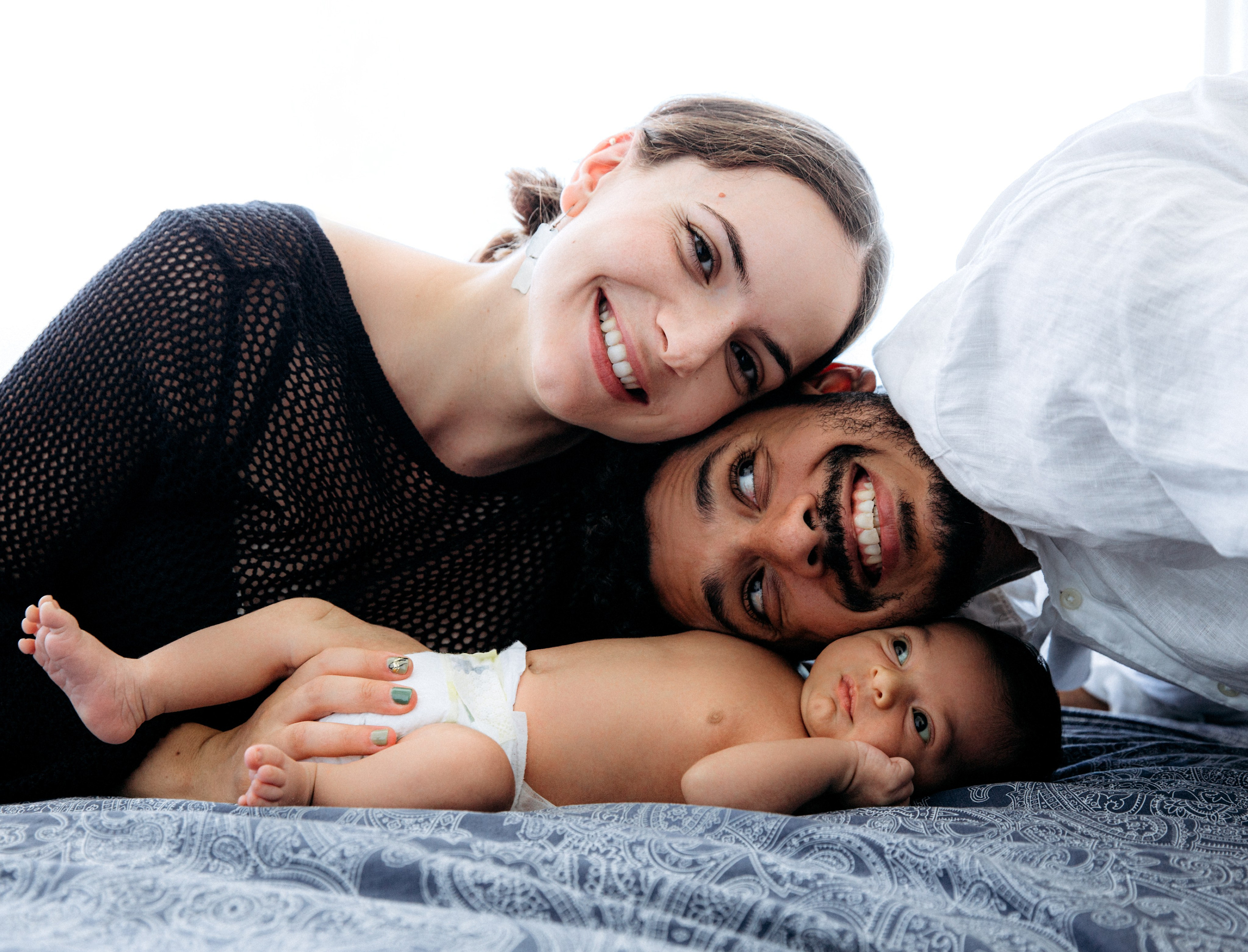 Momento acogedor durante una sesión familiar en interiores en Altea, España — padres sonriendo junto a su recién nacido sobre una manta estampada.