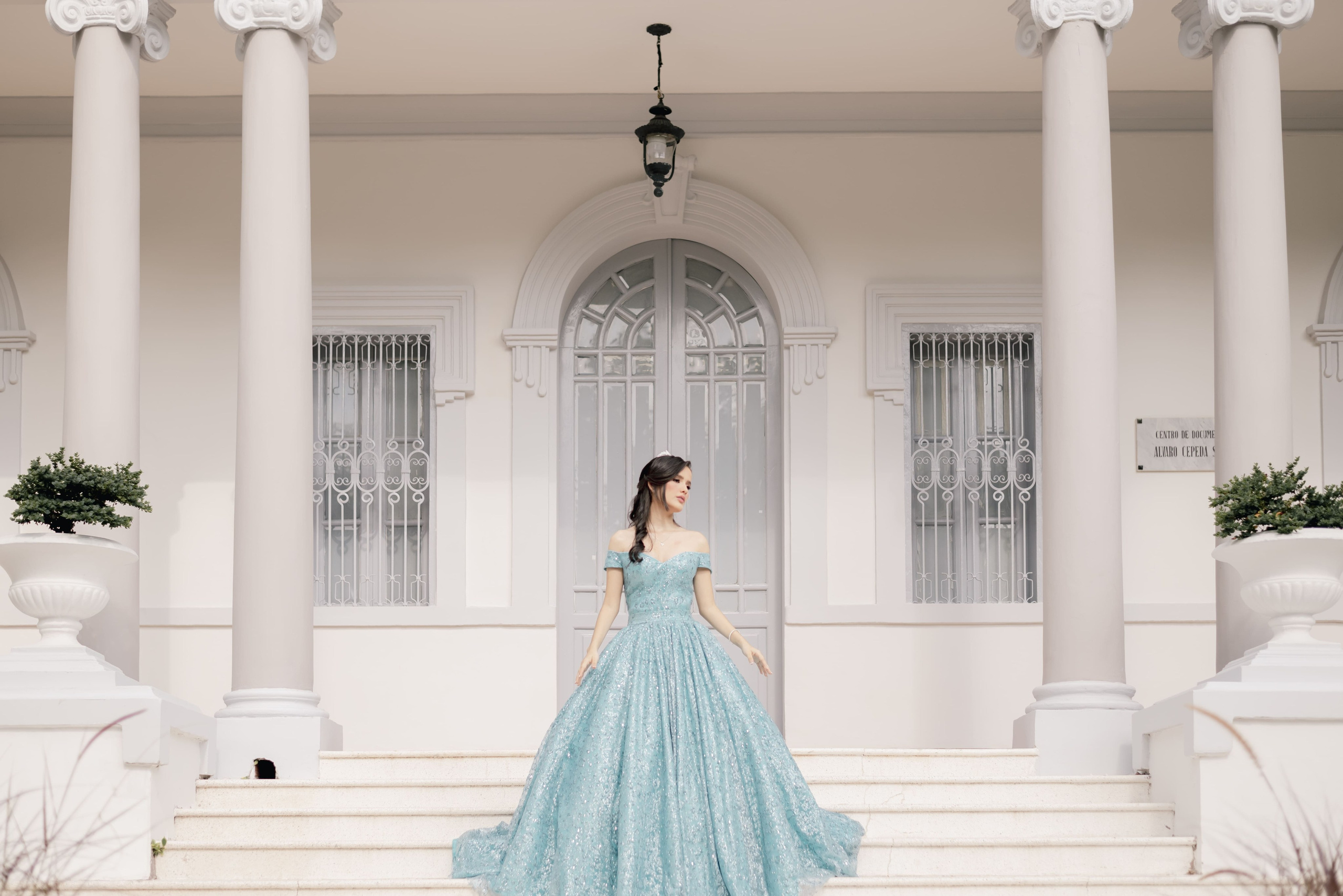 Fotografía de quinceañera de cuerpo completo con vestido azul de princesa en interior elegante con columnas blancas, estilo de ensueño en Barranquilla