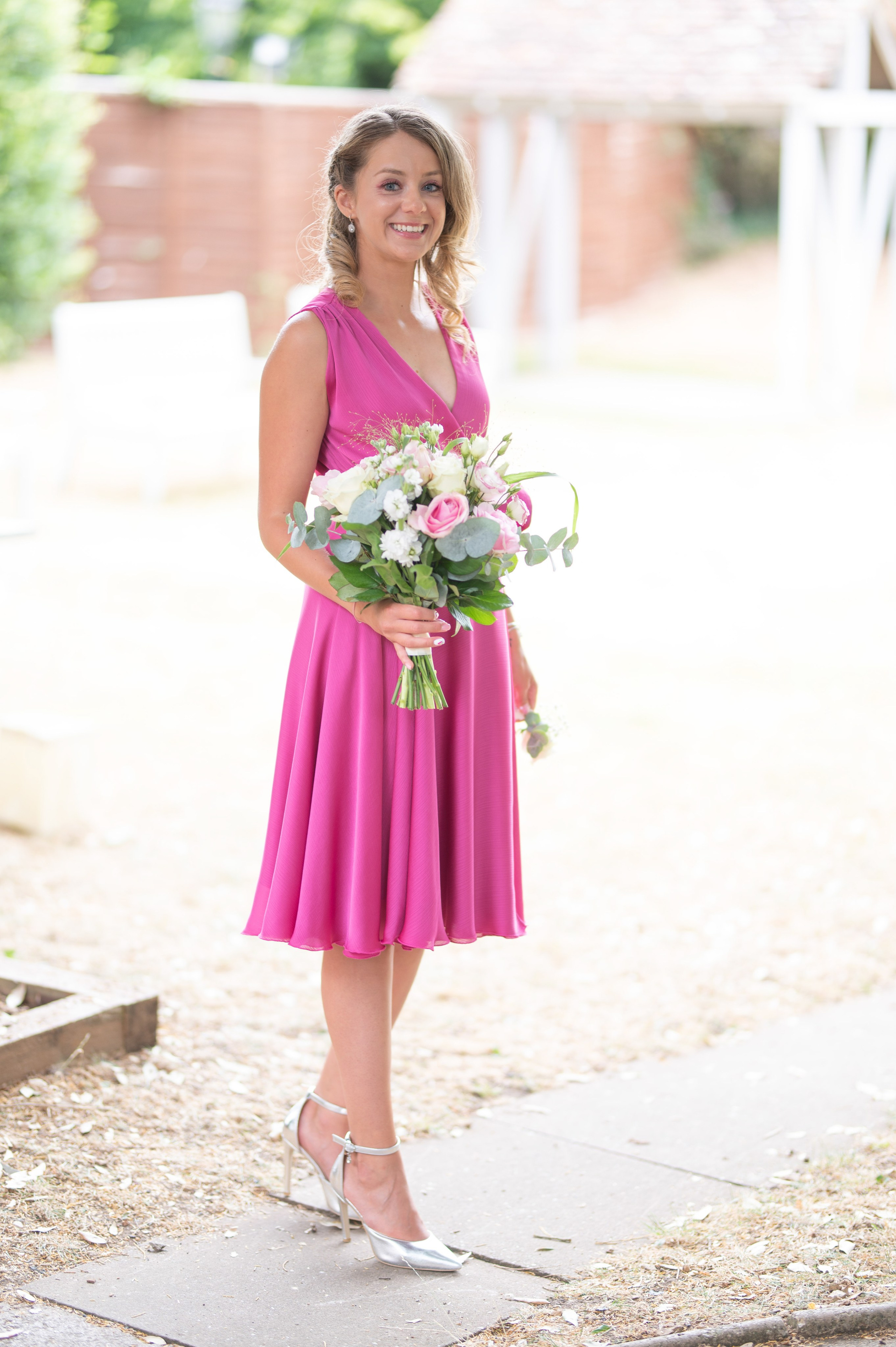 Bridesmaid in a pink dress smiling and holding a bouquet of pink and white roses