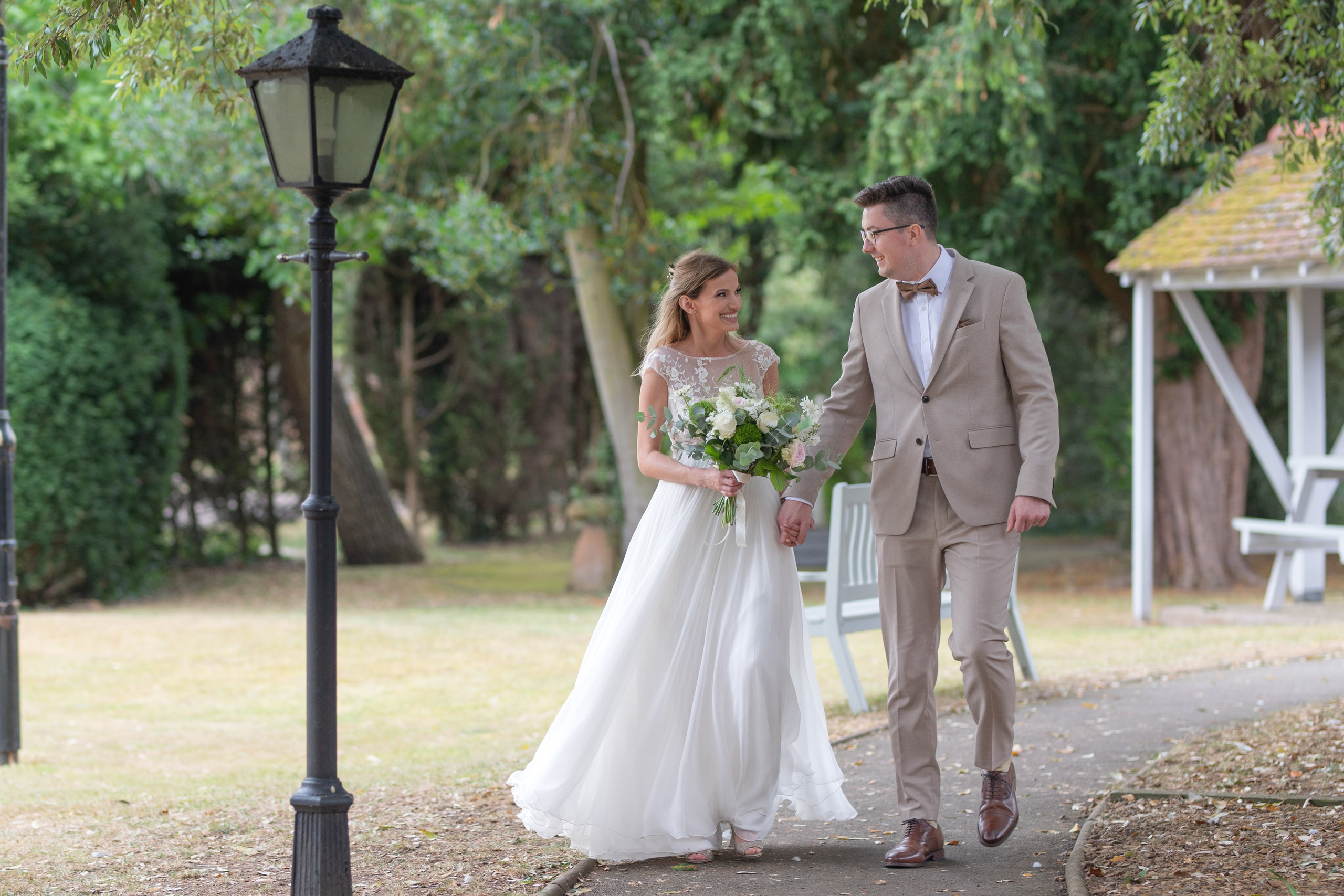 Bride and groom holding hands and smiling at each other while walking through the grounds