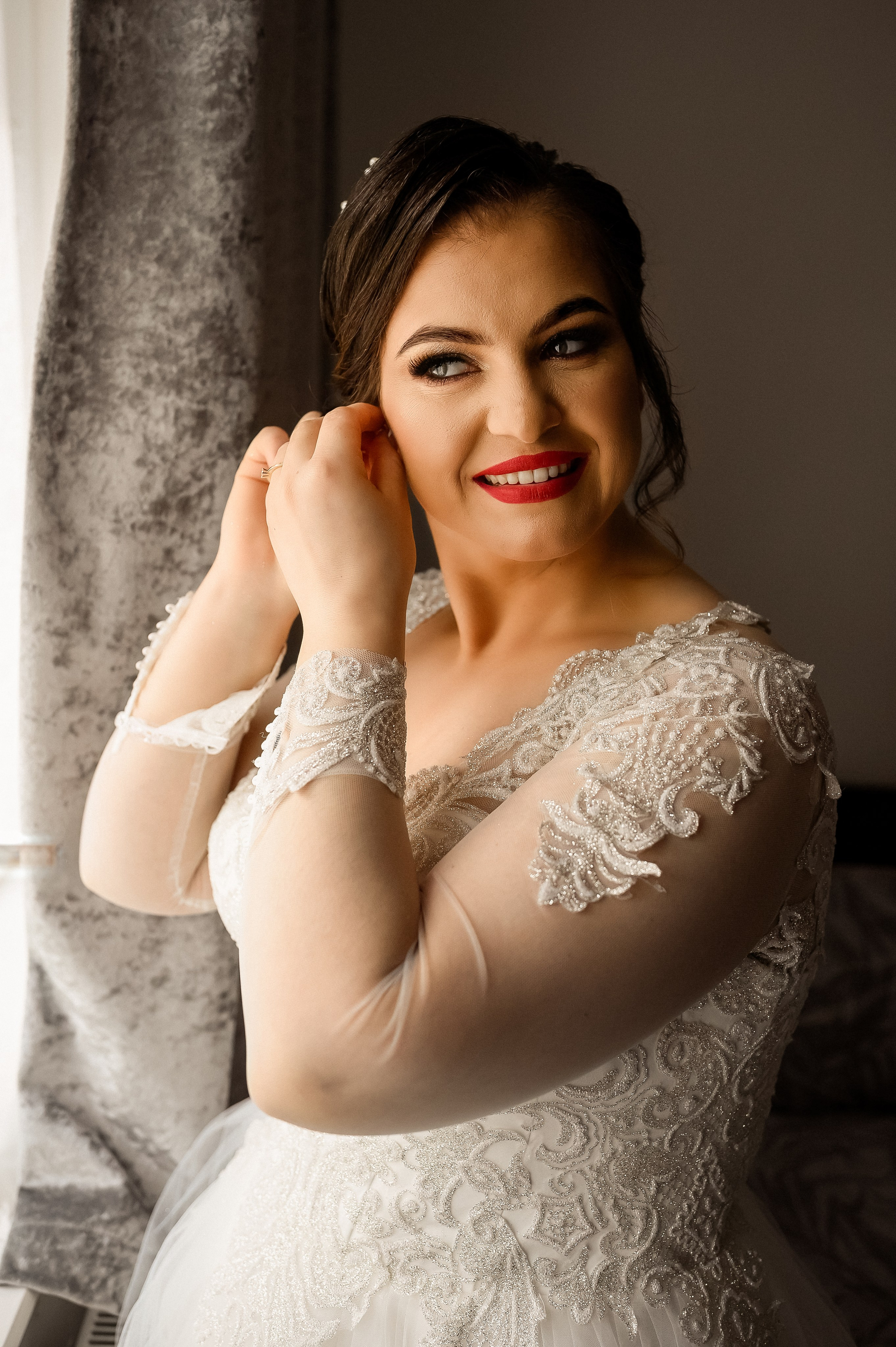 Bride adjusting her earring in warm indoor light before the ceremony