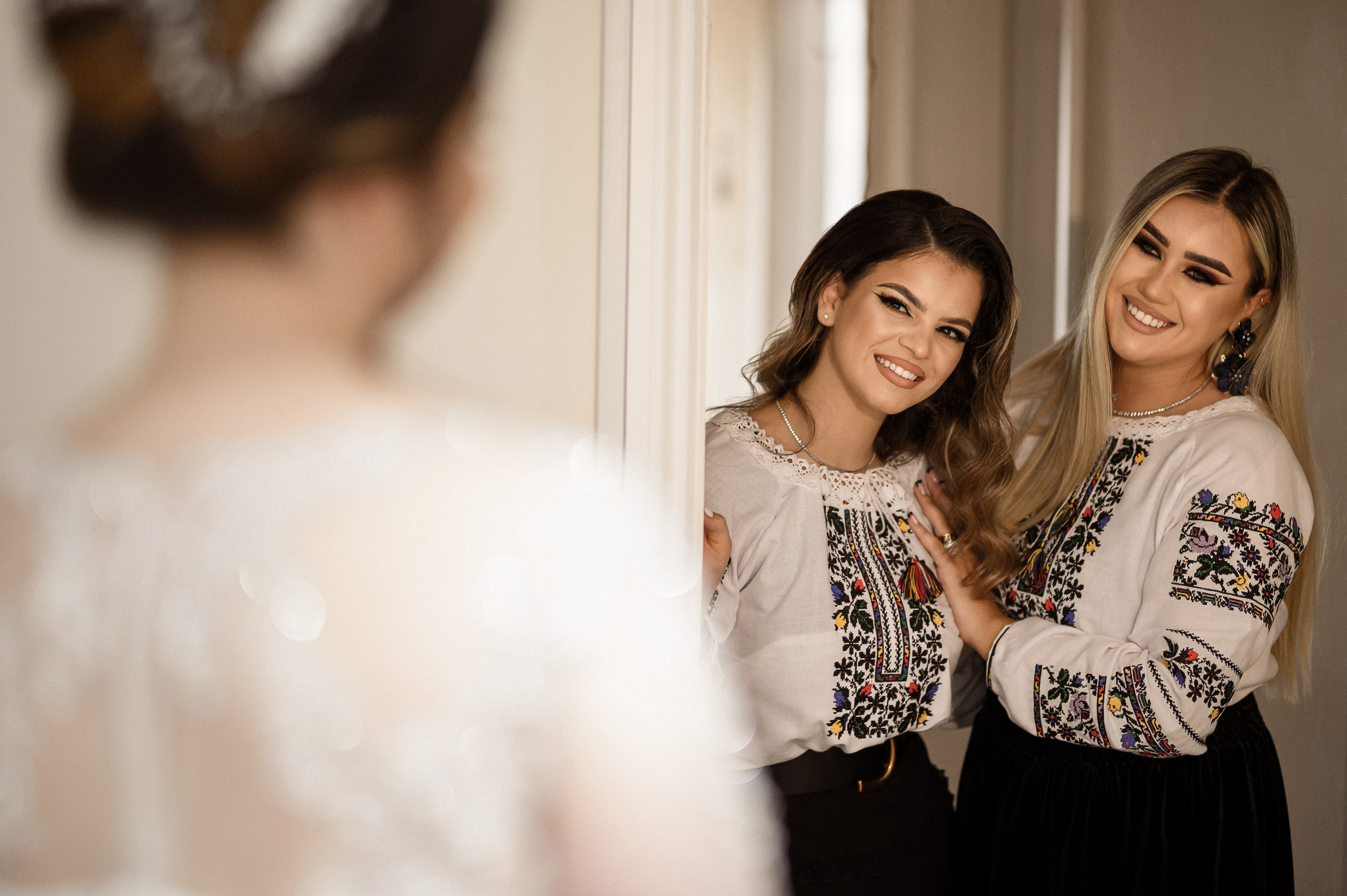 Two bridesmaids in traditional embroidered Romanian blouses standing with the bride