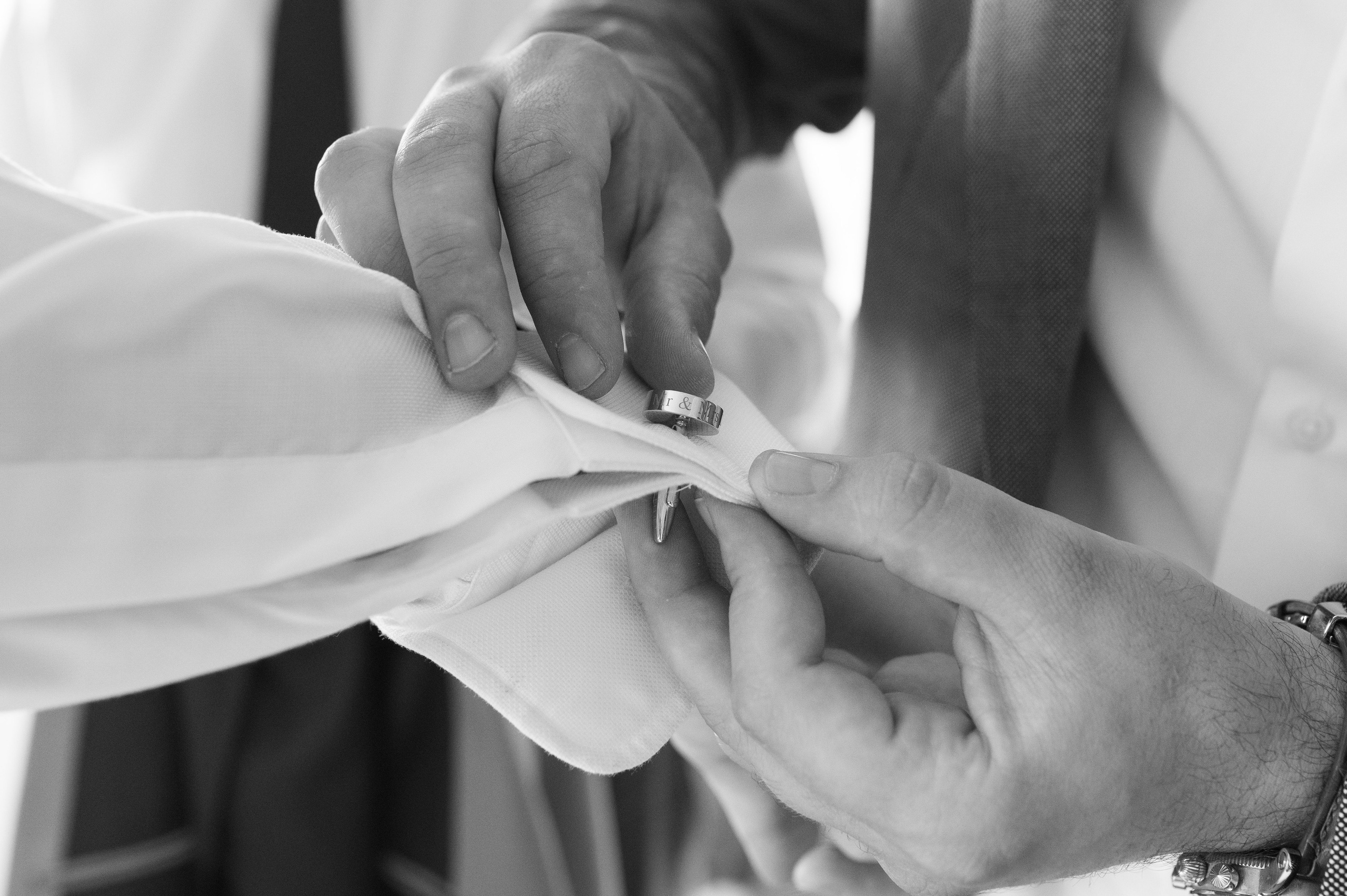 Close-up of the groom's personalised "Mr & Mrs" cufflinks being fastened (black and white)
