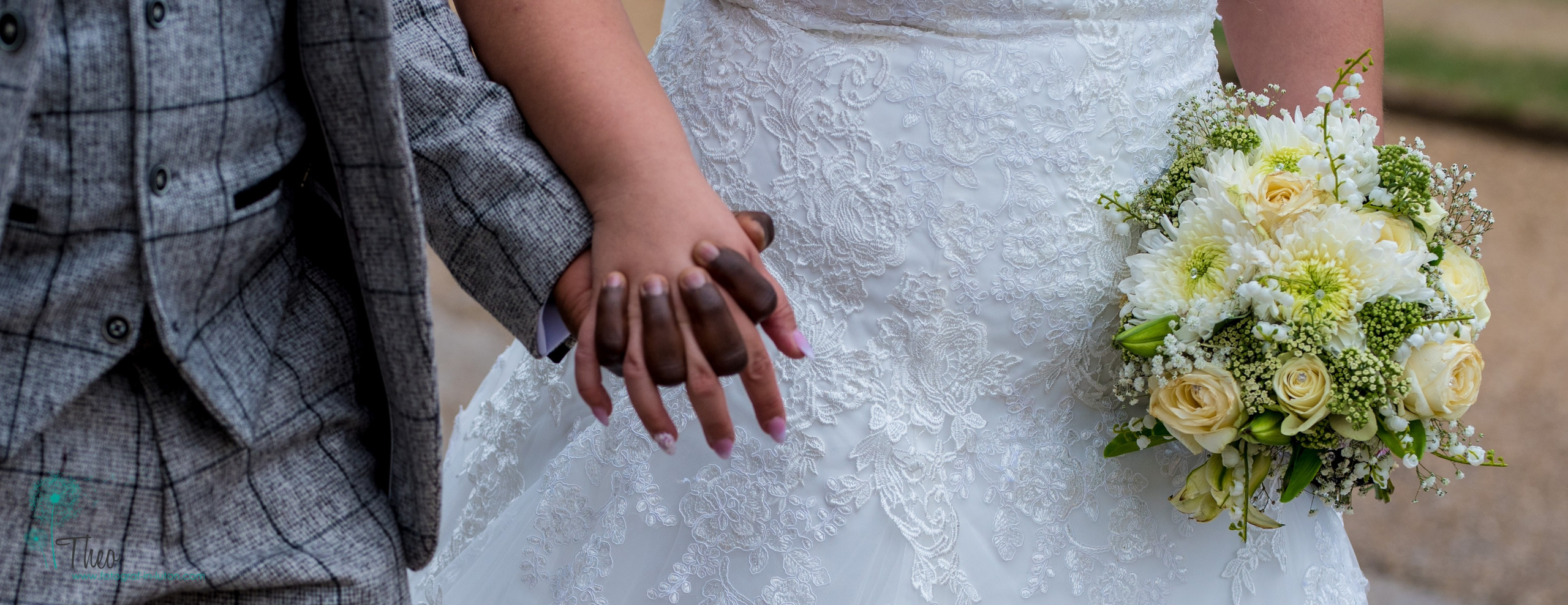 A close-up of the bride and groom's joined hands beside her bouquet of cream roses and white chrysanthemums